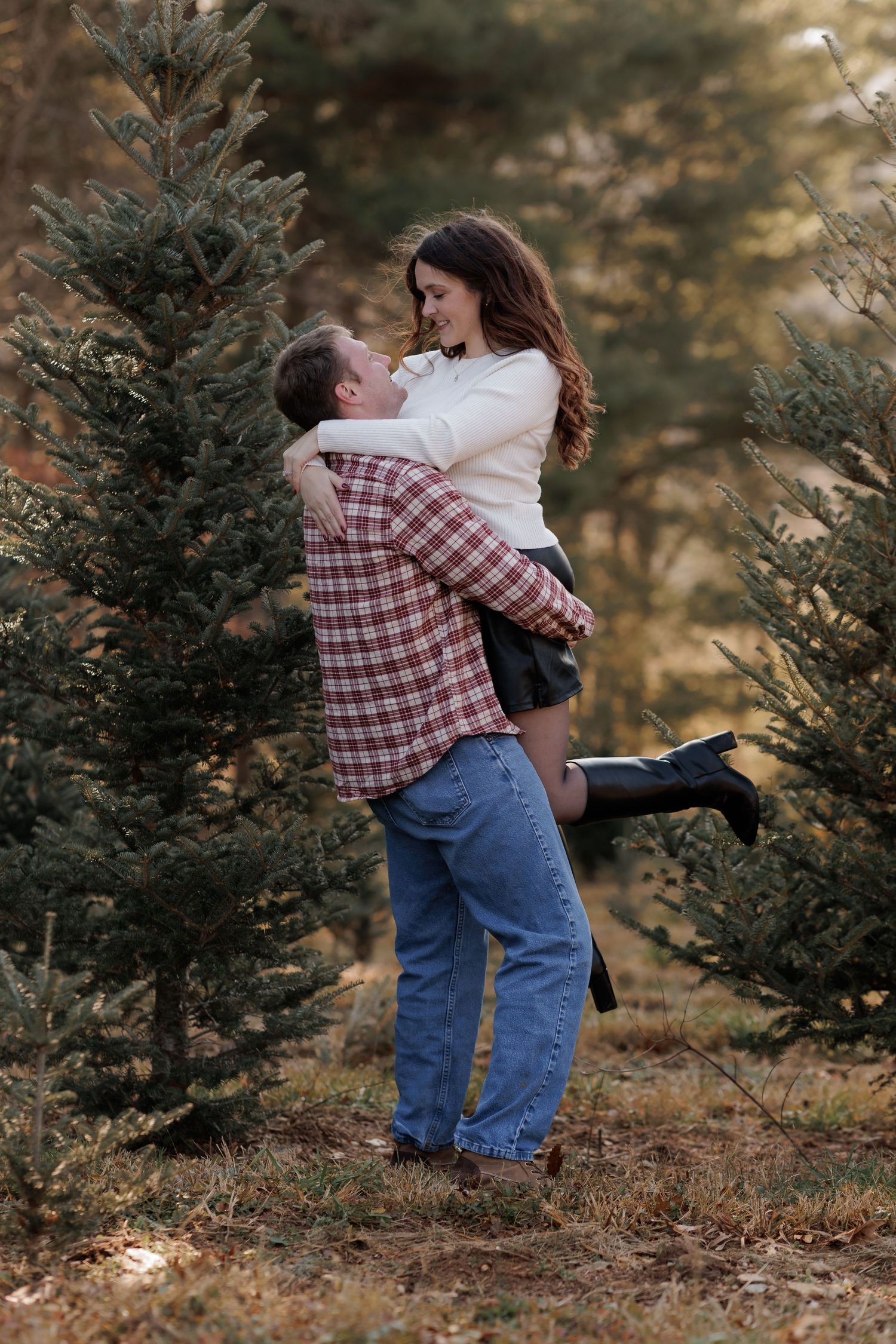 Romantic couple embraces among evergreen trees during outdoor photo session.