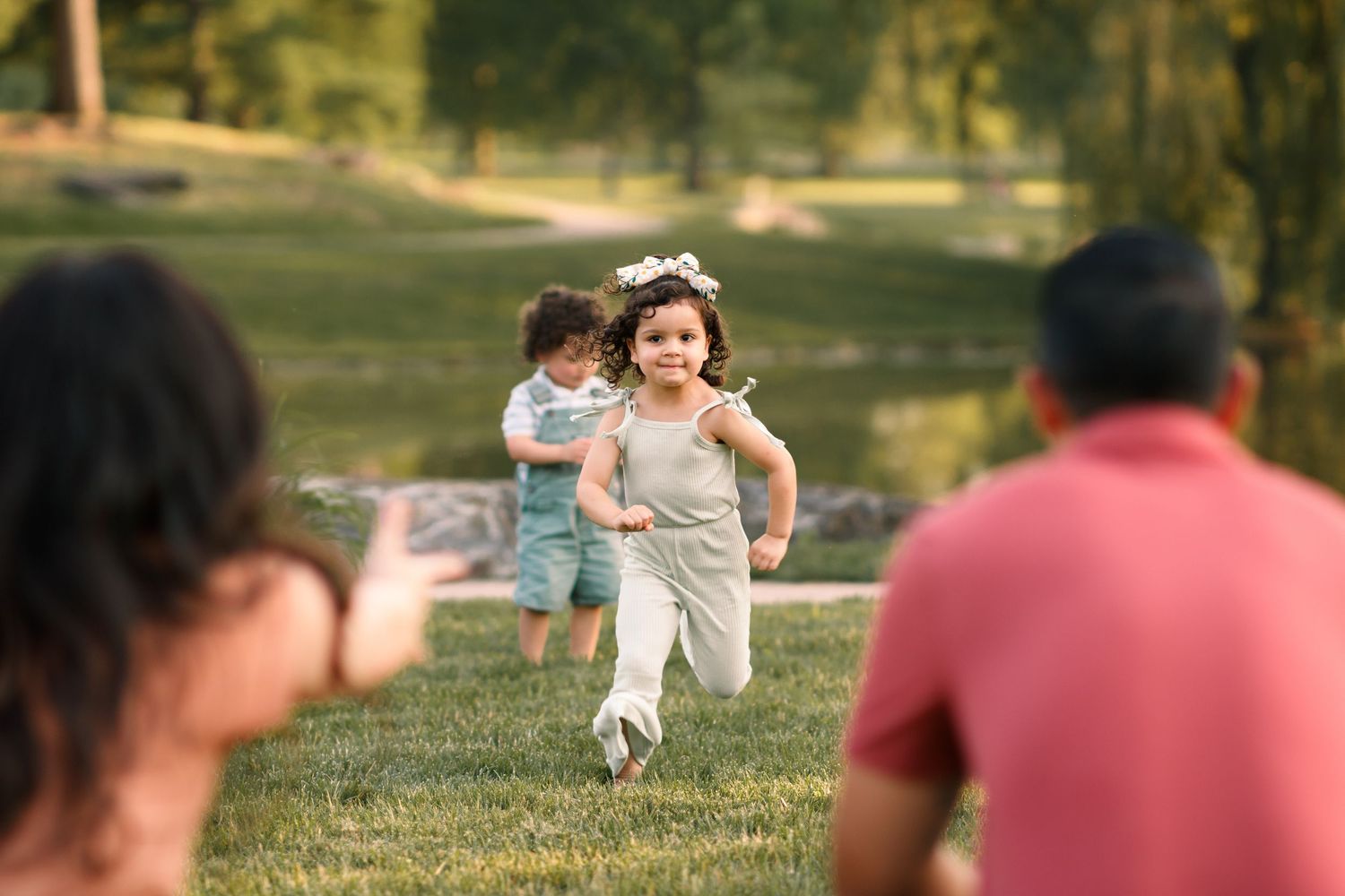 A young child runs joyfully across a grassy lawn while others watch in the background.
