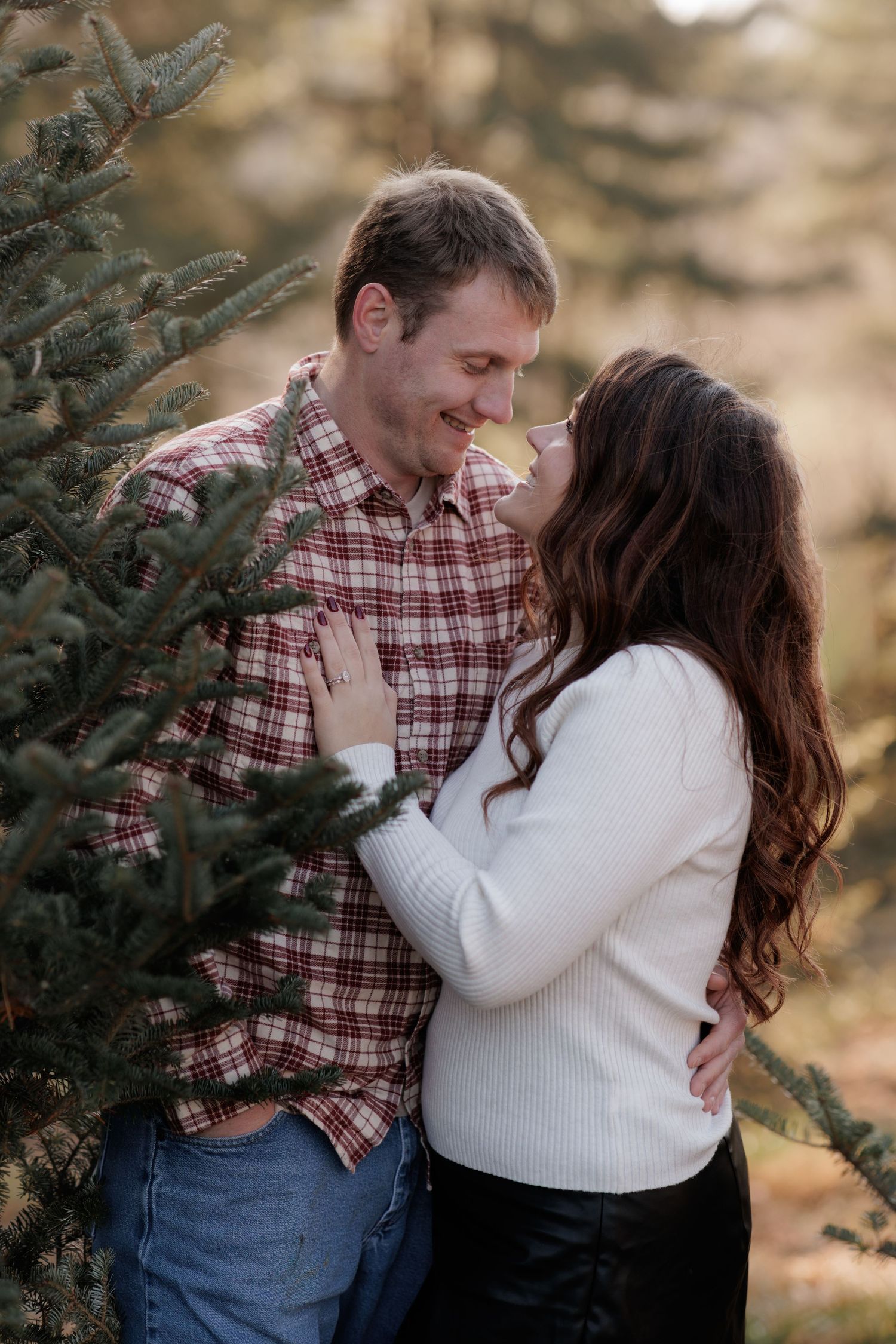 Intimate moment between couple surrounded by pine trees during winter photoshoot.