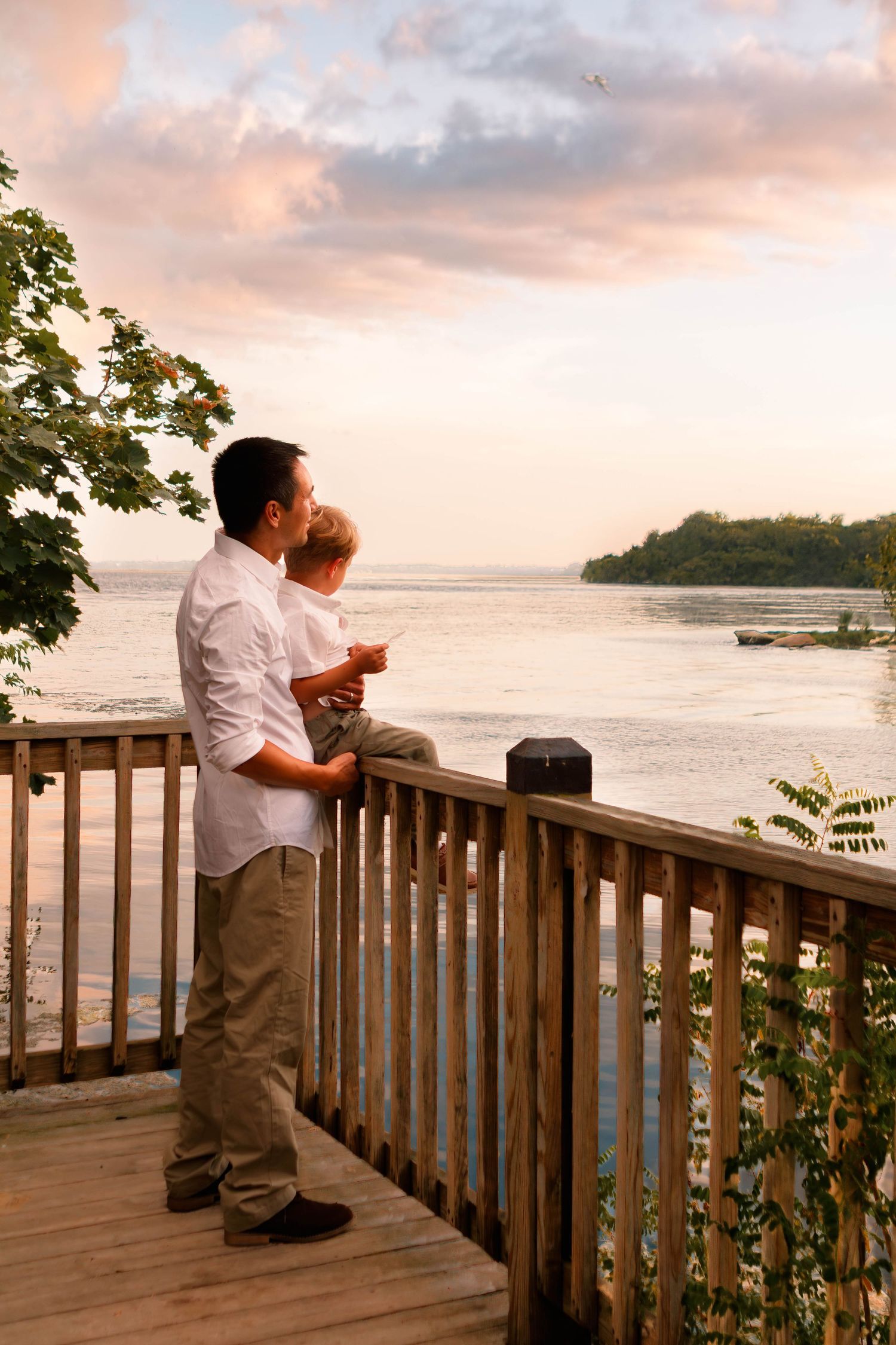 A peaceful sunset view from a wooden deck overlooking a waterfront.