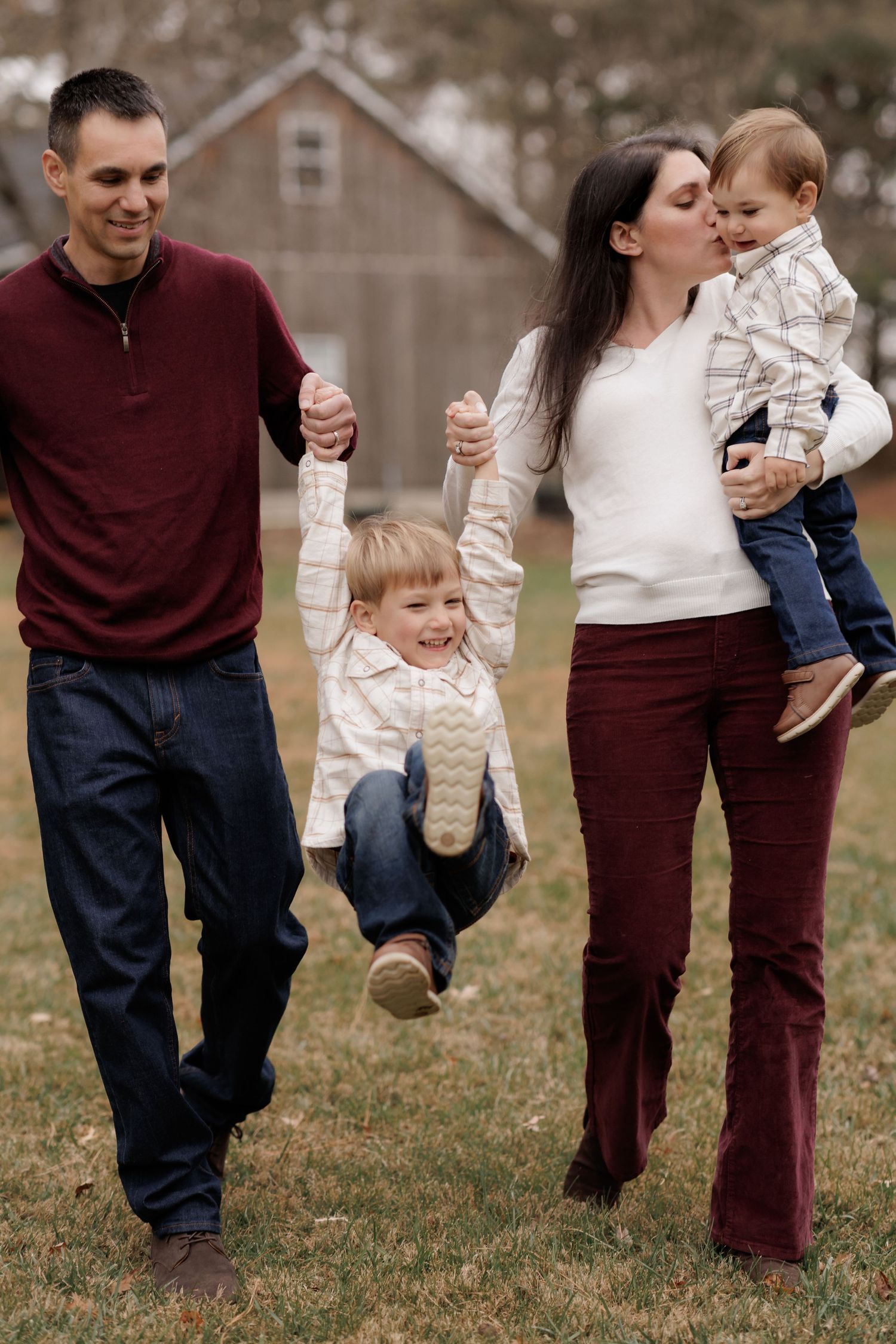 Family playing and walking together in a grassy field wearing coordinated burgundy and white outfits.