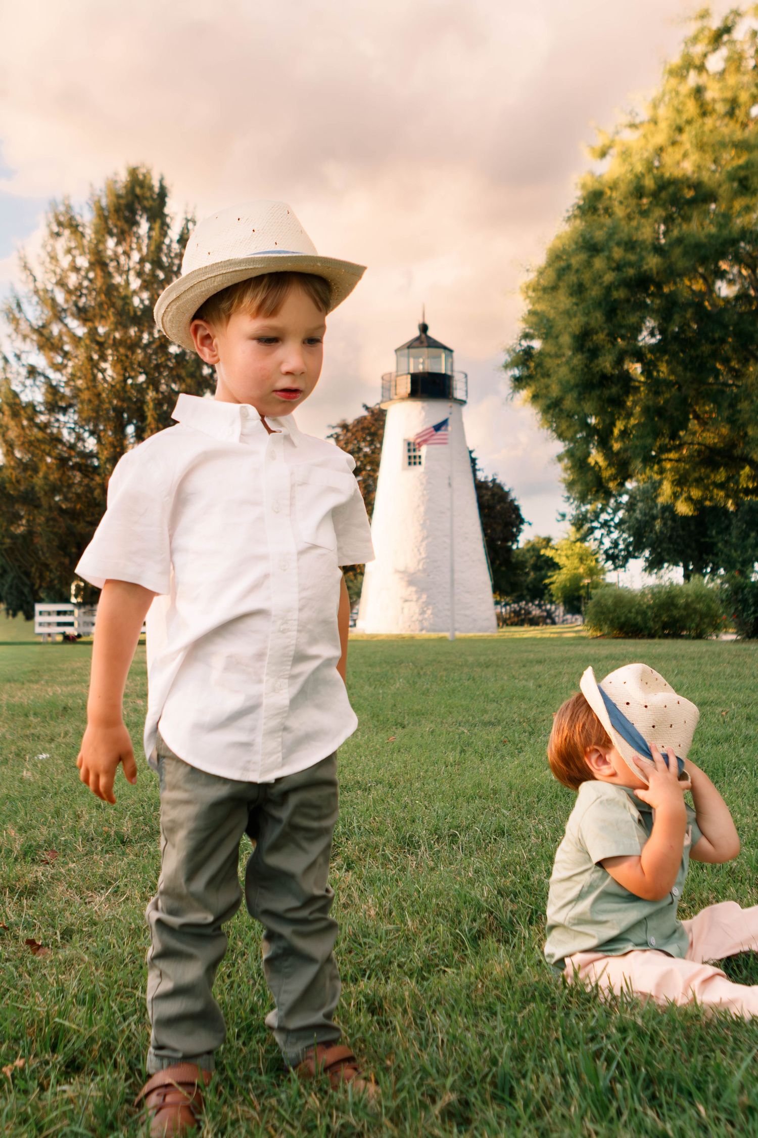 Children in sun hats near a white lighthouse on a grassy lawn.
