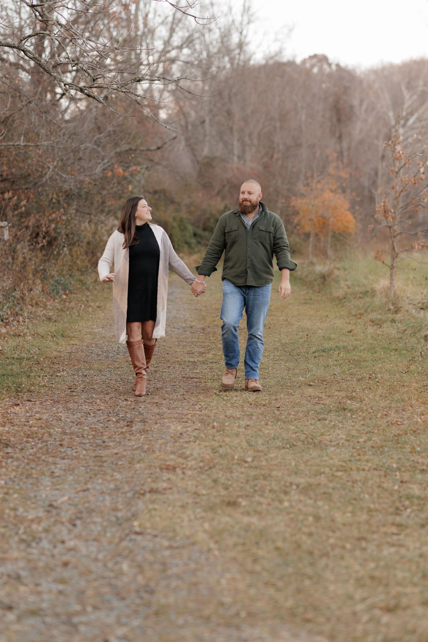 Couple walks hand in hand down autumn trail in casual outdoor wear.