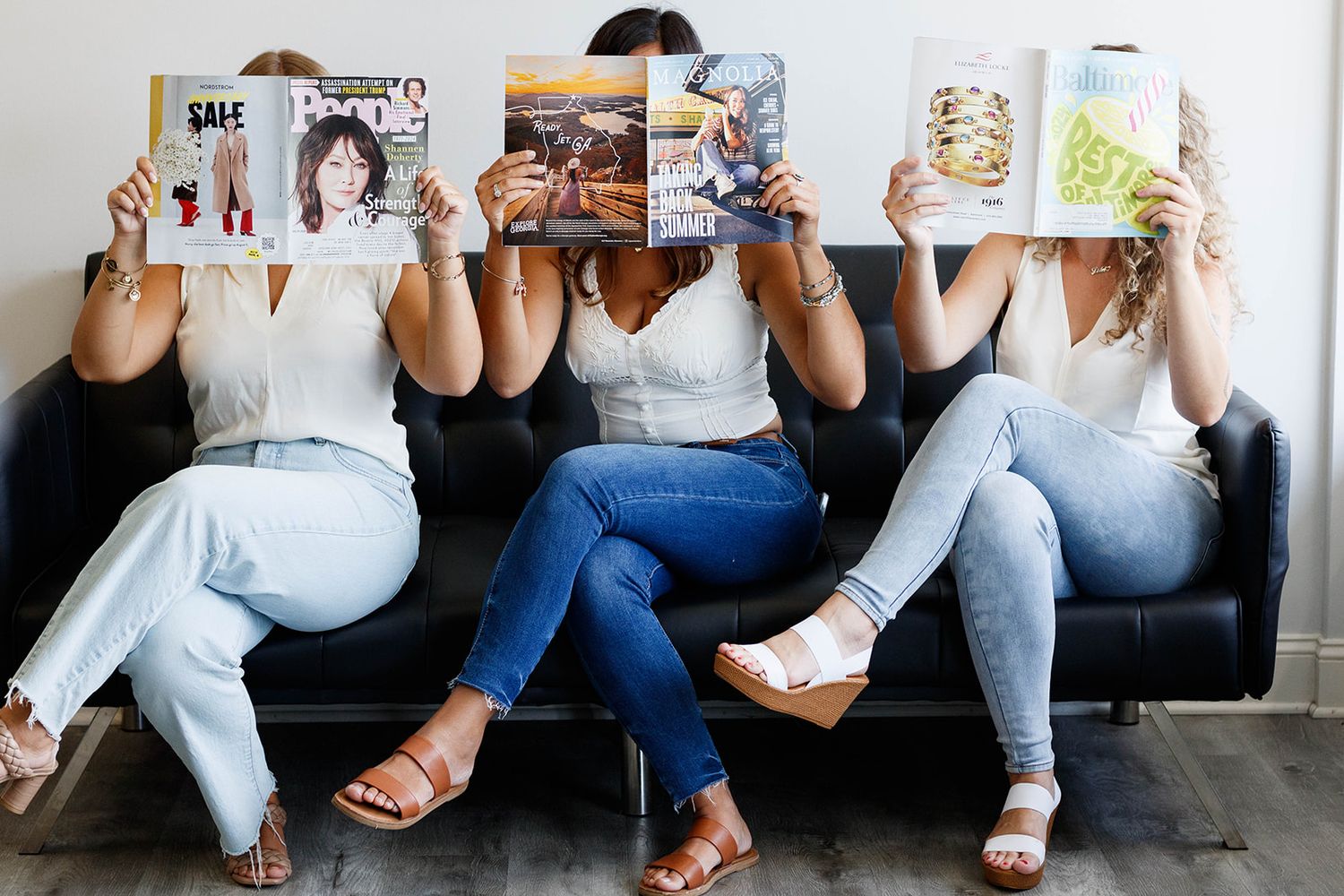 Group of people sitting on couch holding magazines in front of their faces.