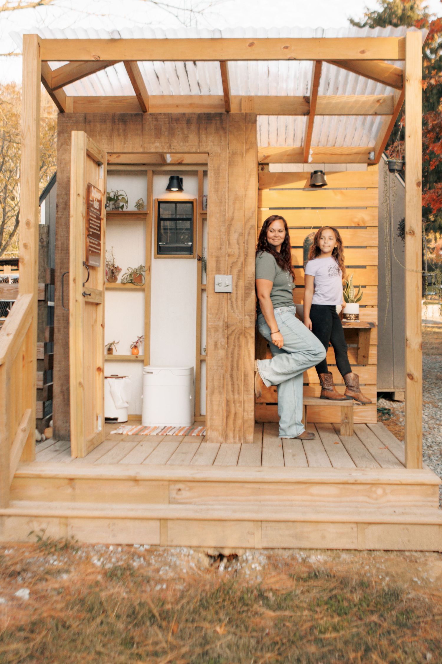 A rustic wooden outdoor structure with a transparent roof and people sitting on wooden steps.