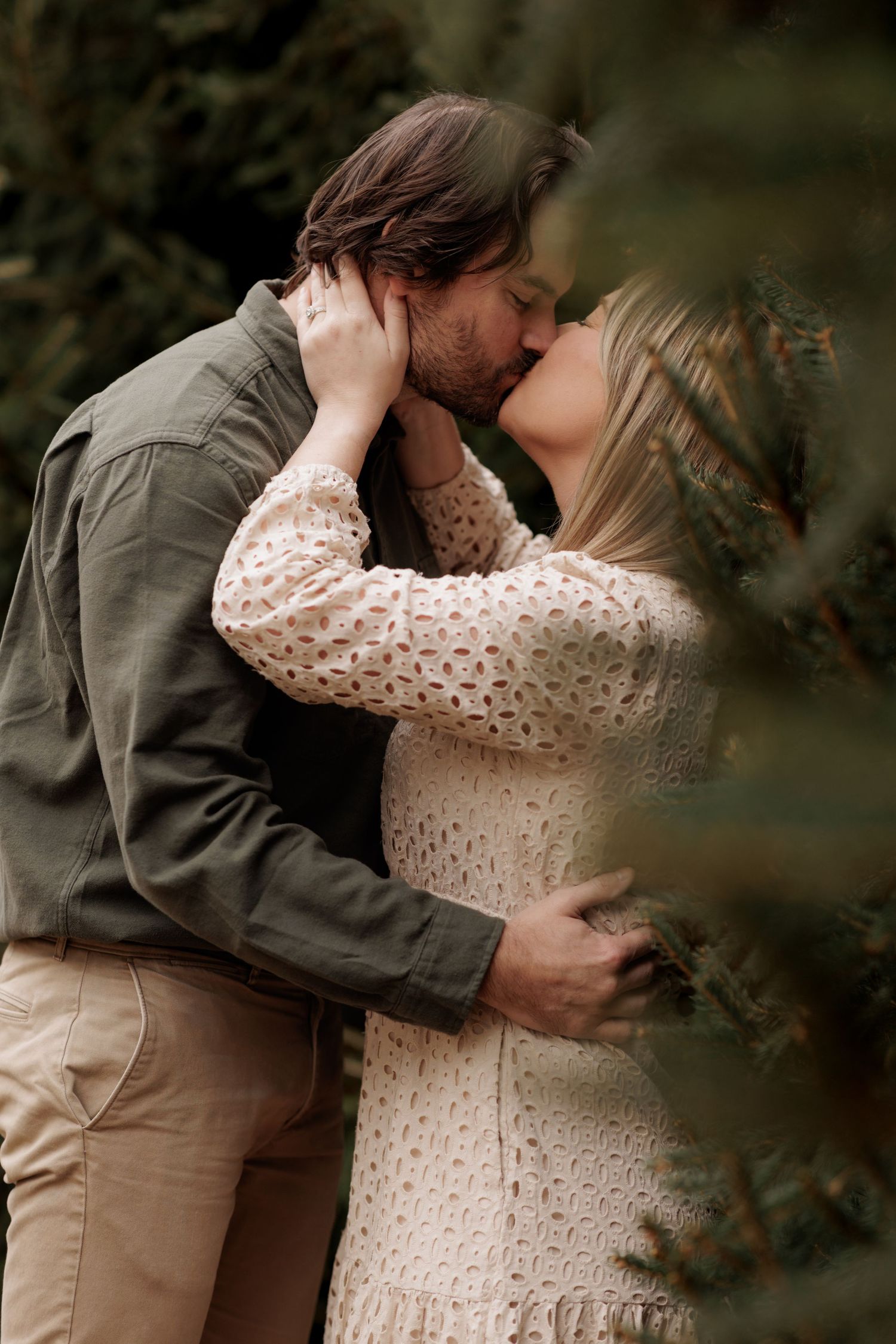 Romantic couple embraces in an outdoor setting wearing a lace dress and olive jacket.