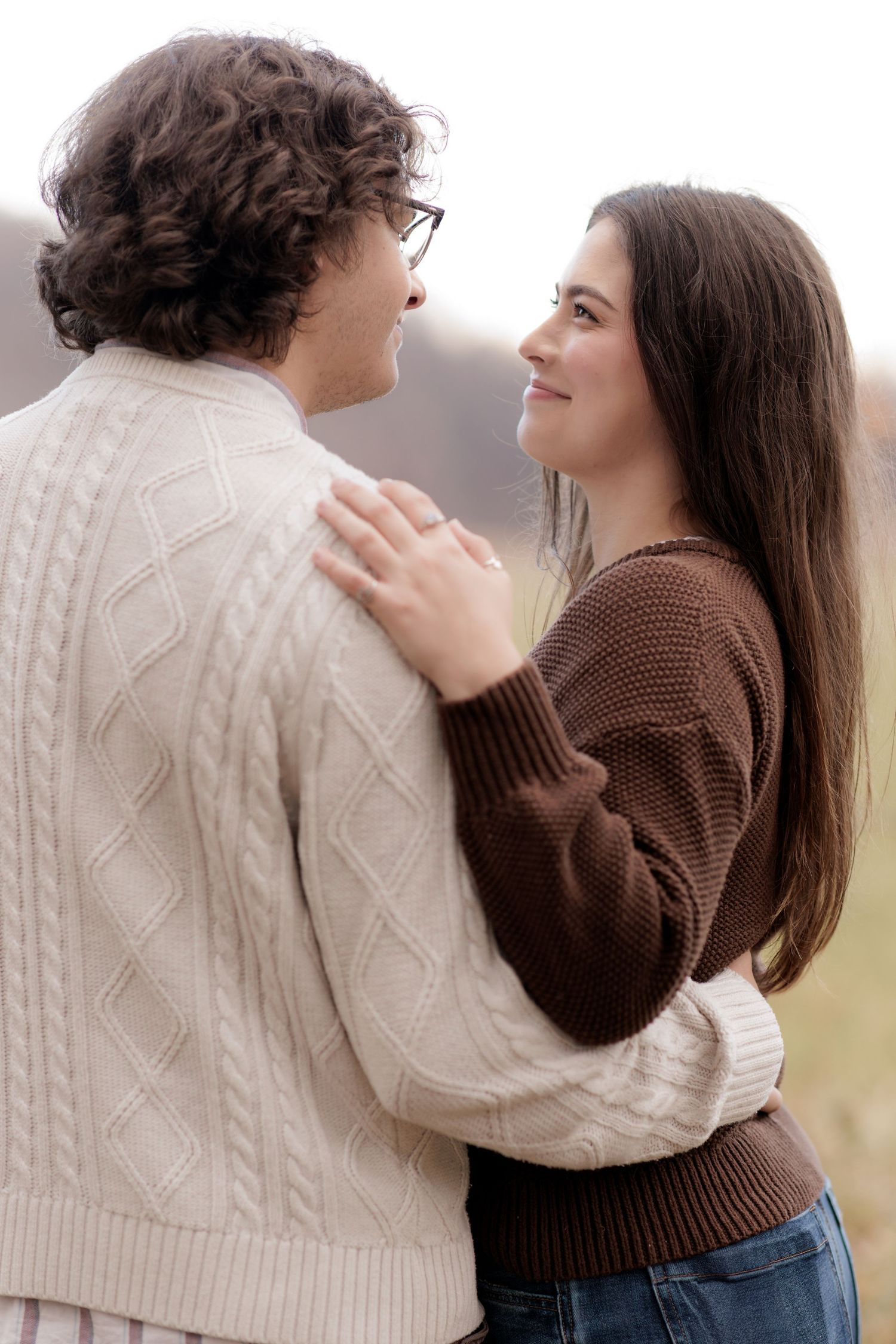 Couple in cozy sweaters share tender moments during outdoor photoshoot.