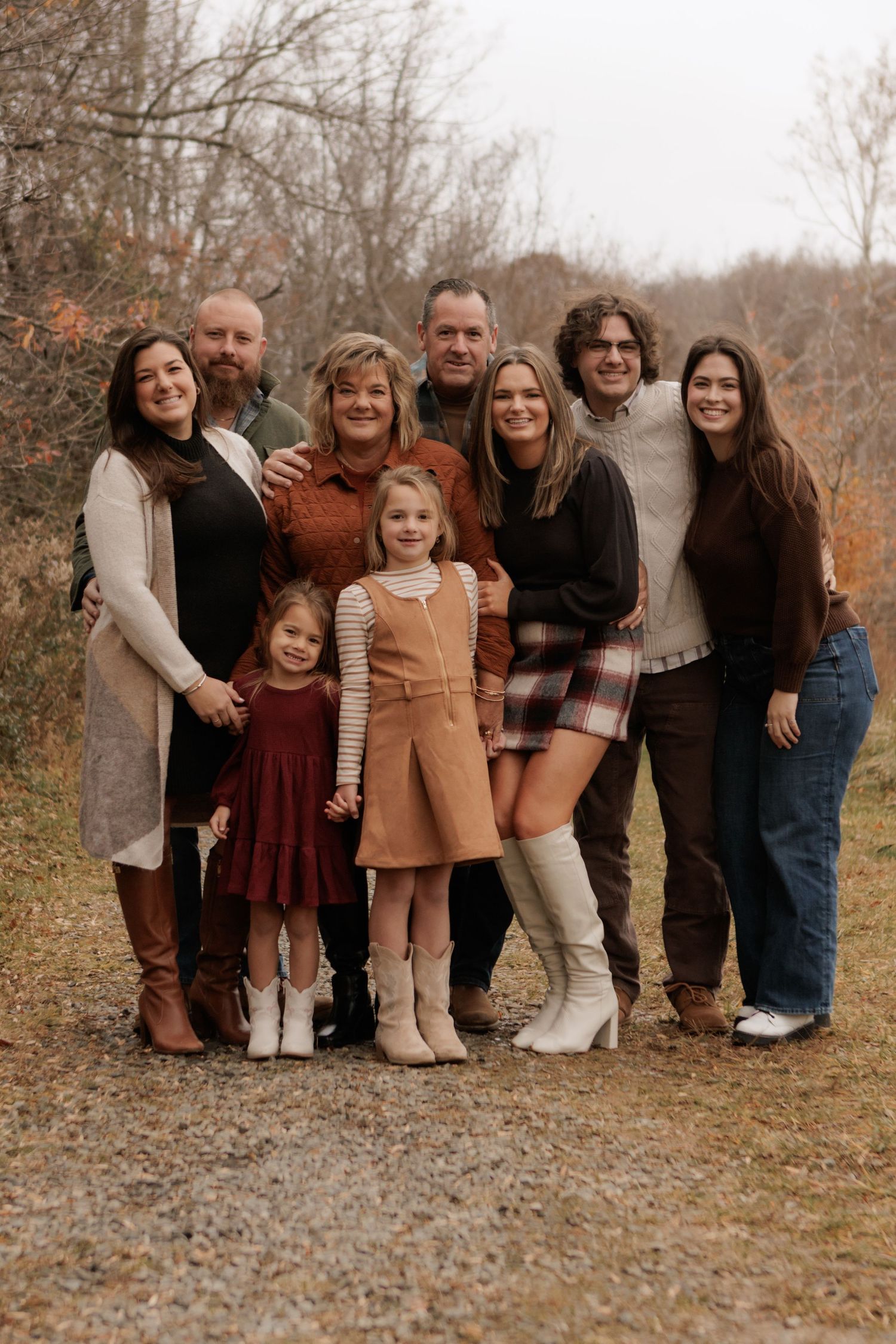 Multi-generational family group poses together on a gravel path during autumn.
