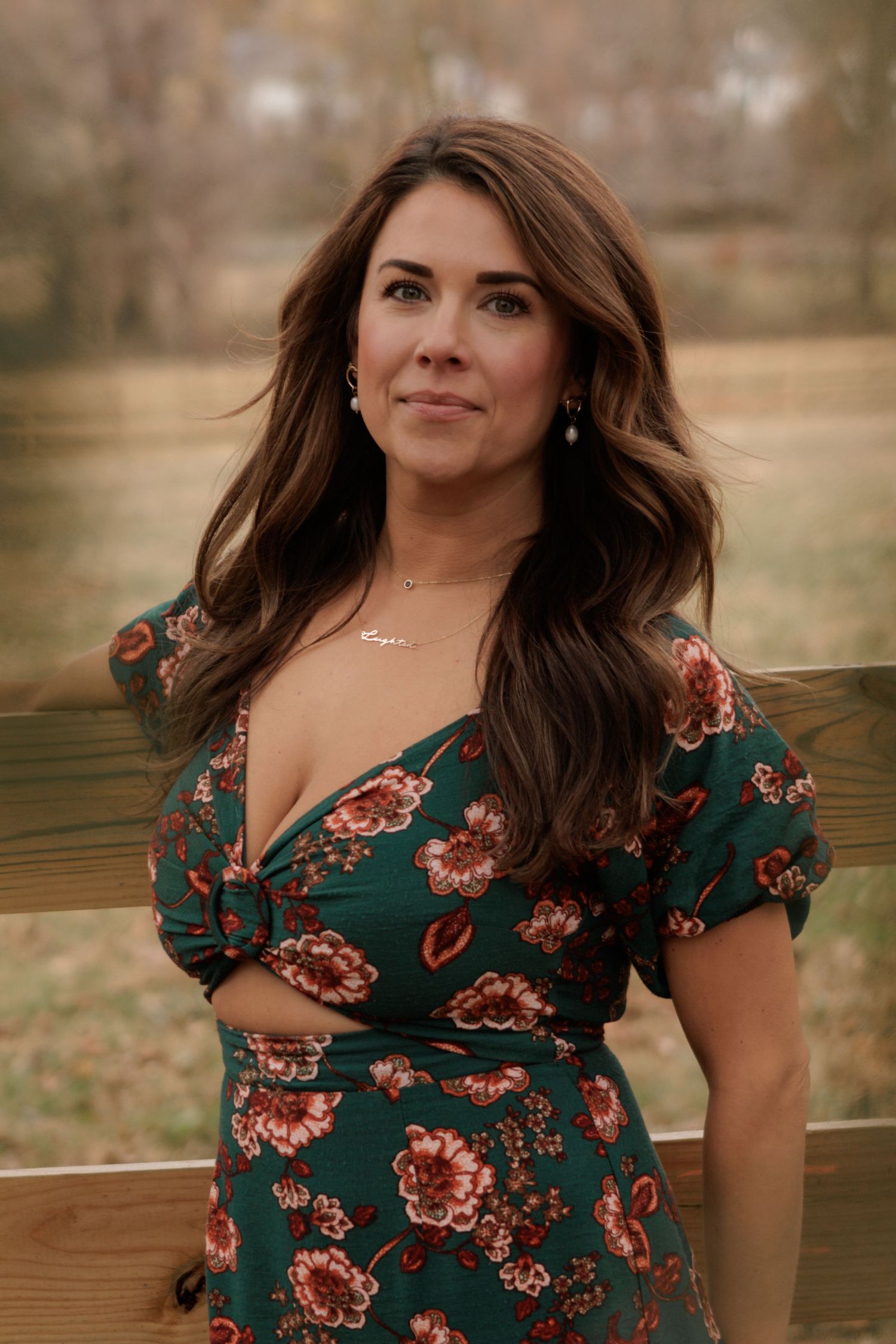 Woman in floral green dress smiling outdoors in natural lighting.