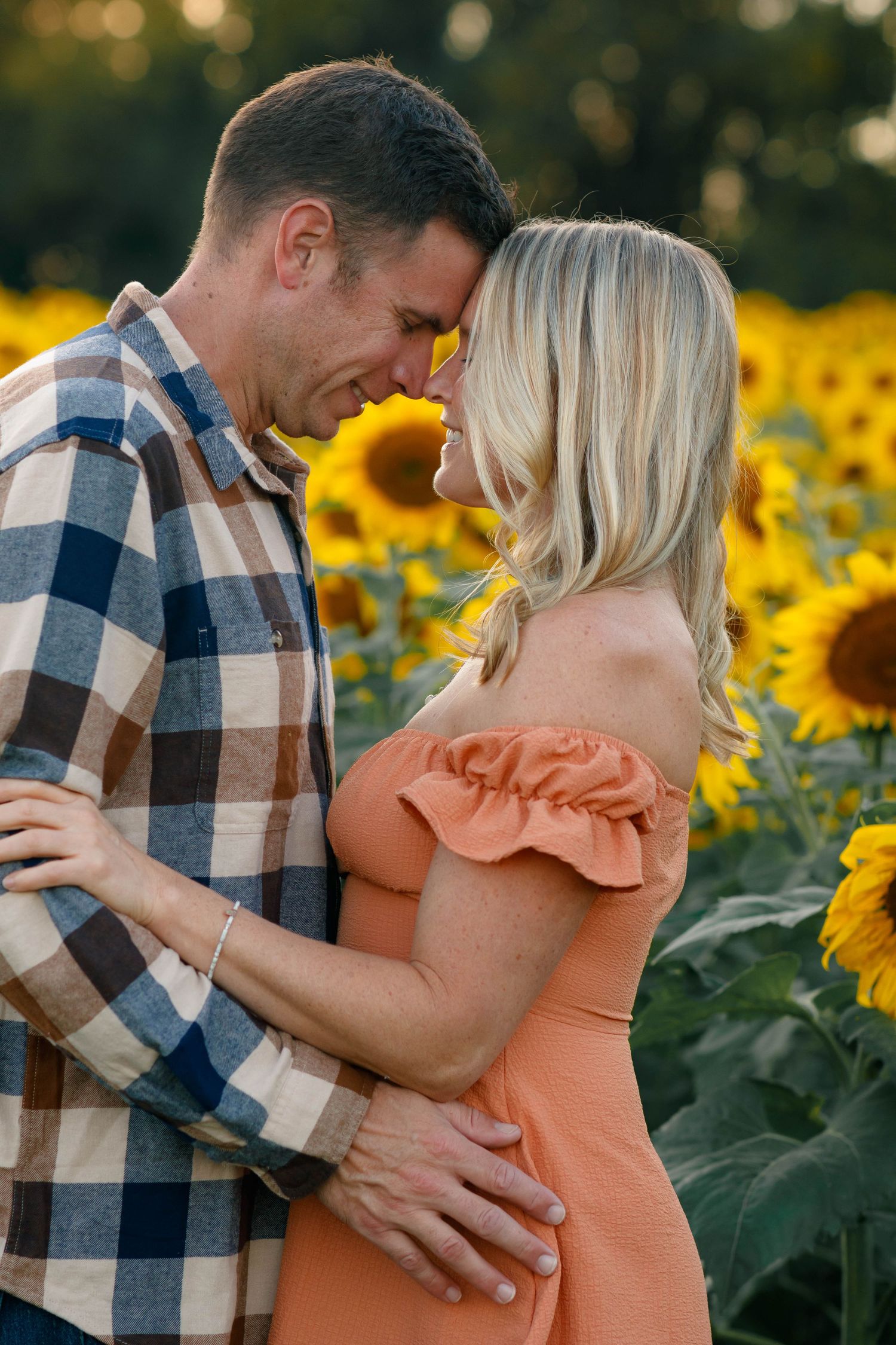 A romantic couple embraces in a vibrant sunflower field during a summer photoshoot.