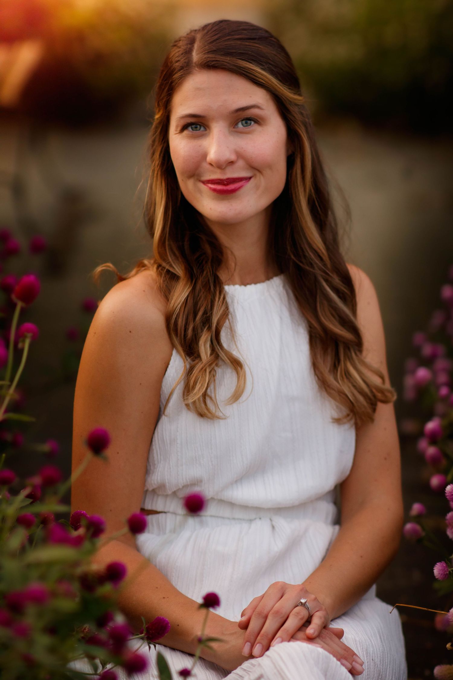 Portrait in white dress surrounded by purple flowers in garden at sunset.