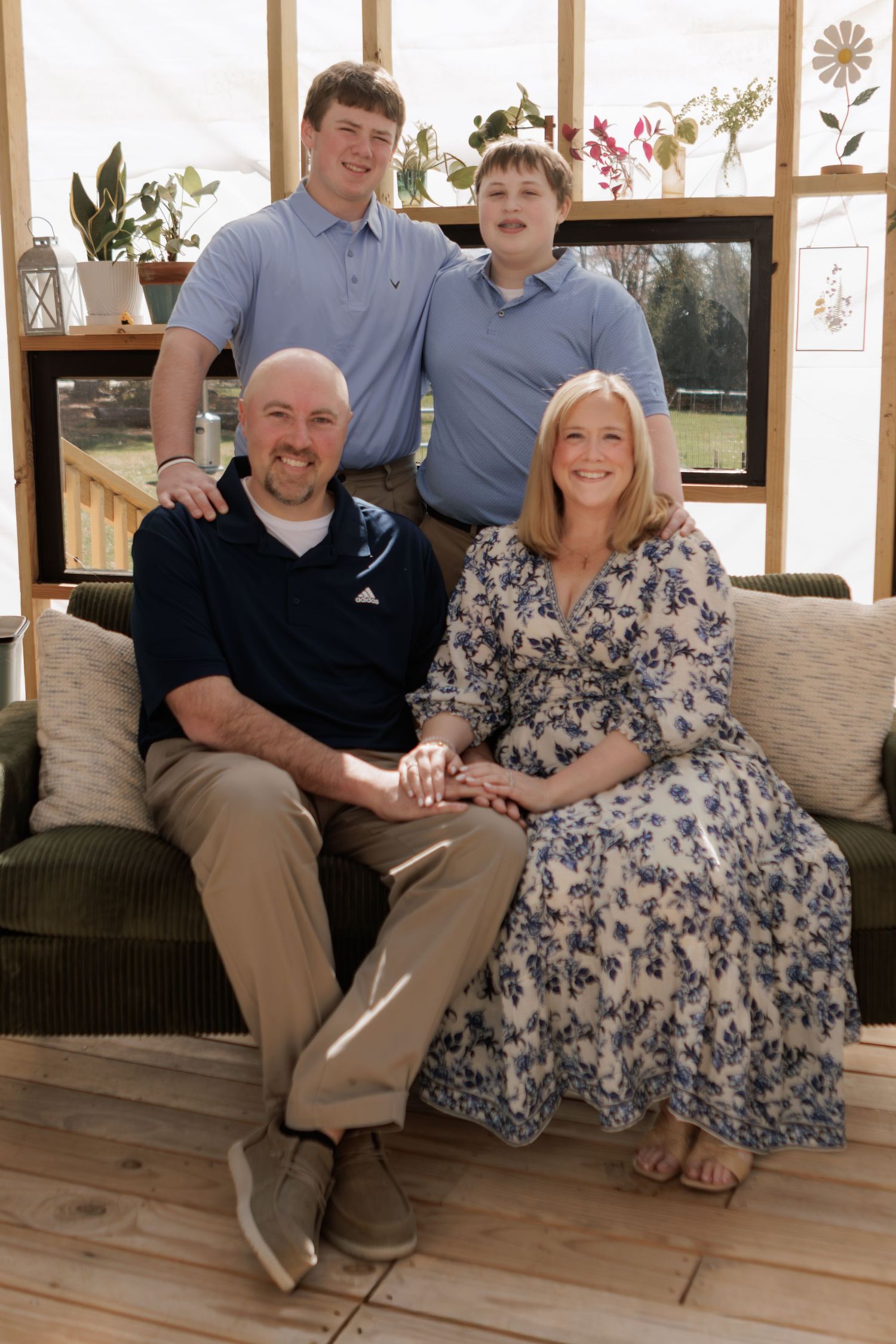 Happy family of four posing together indoors, two parents seated on a couch with two teenage sons standing behind them.