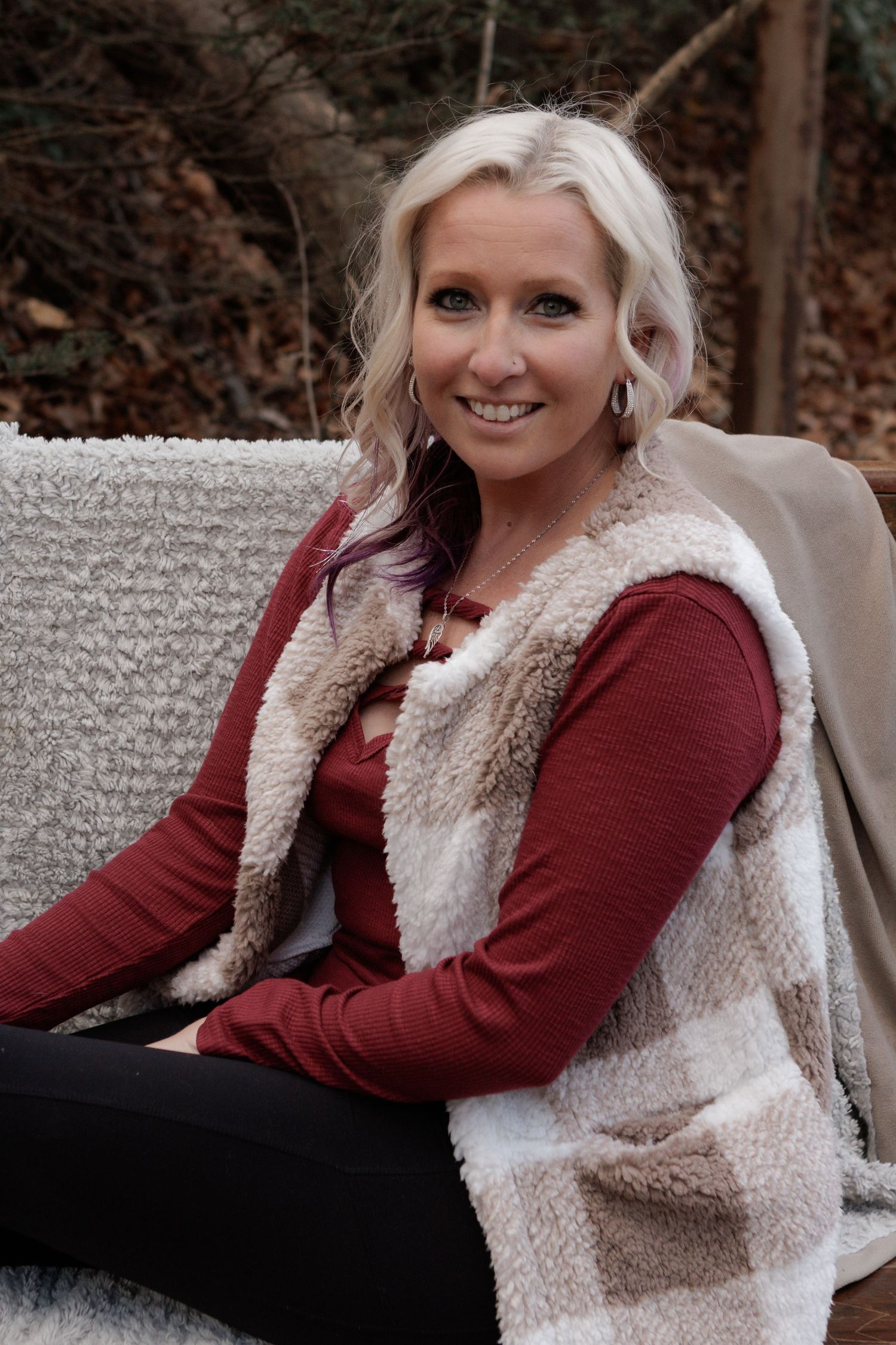Person wearing burgundy sweater and fur vest relaxes on gray couch.