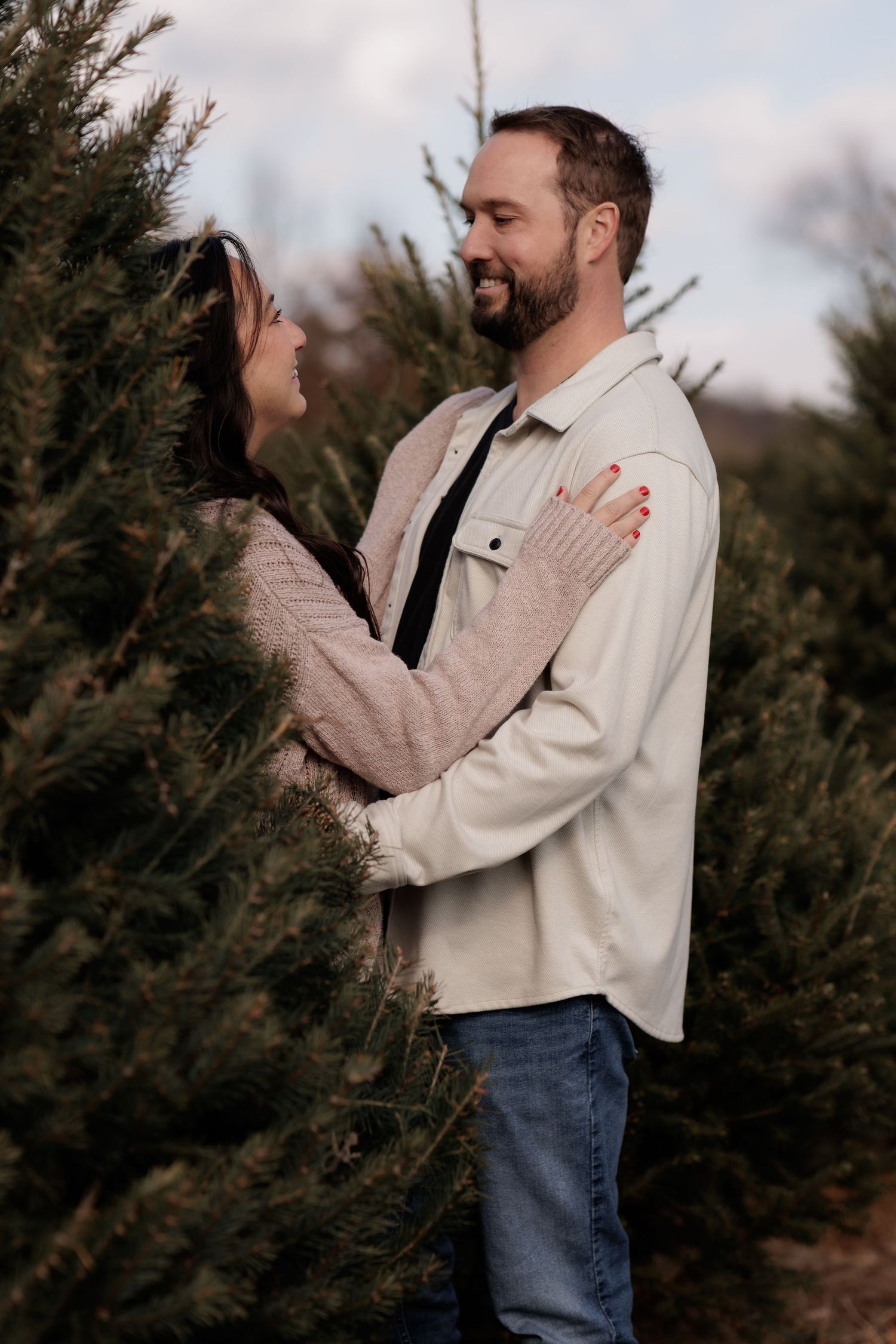 Couple sharing romantic moments among evergreen trees at dusk.
