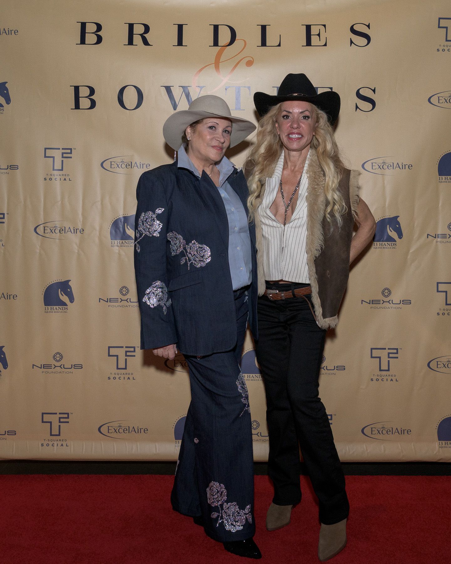Two women in western attire posing at Bridles and Bowties red carpet event.