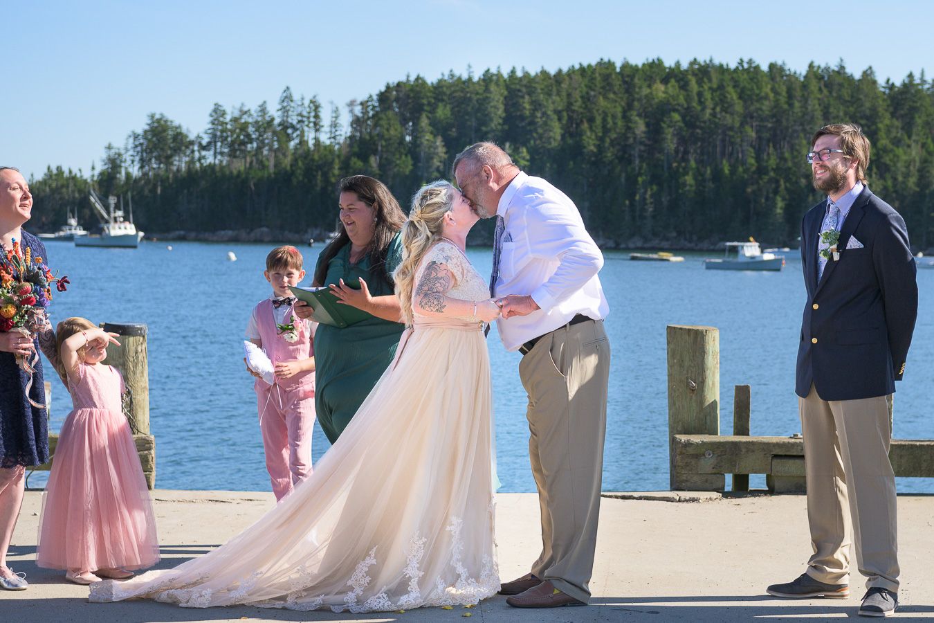 Bride and groom share first kiss at waterfront wedding ceremony.