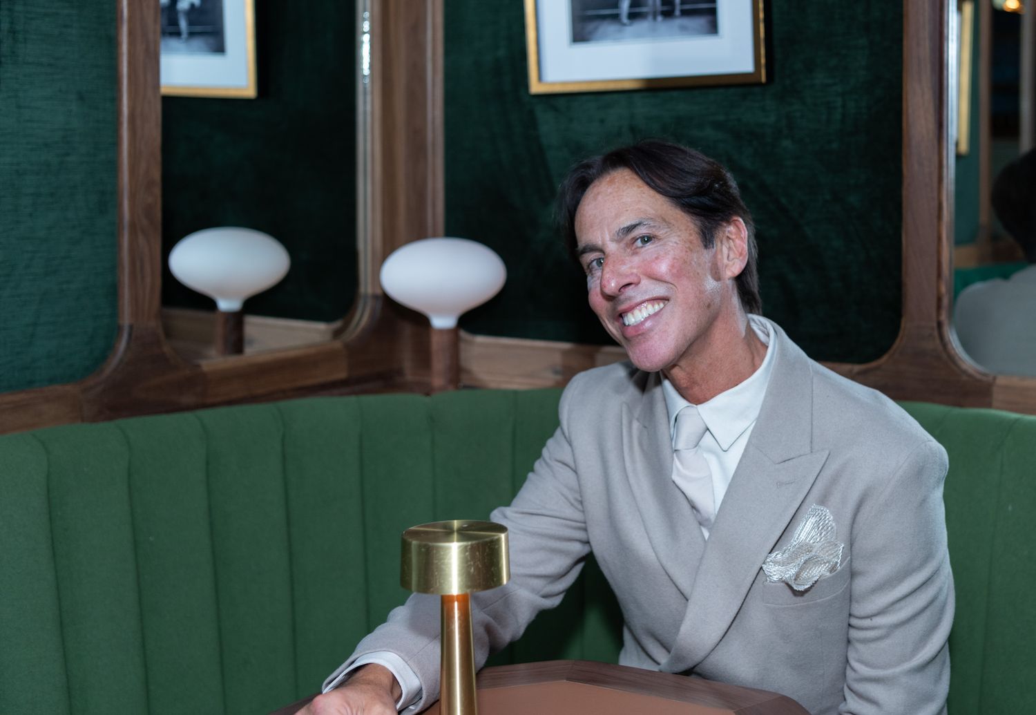 Smiling man in gray suit relaxing in green velvet restaurant booth.