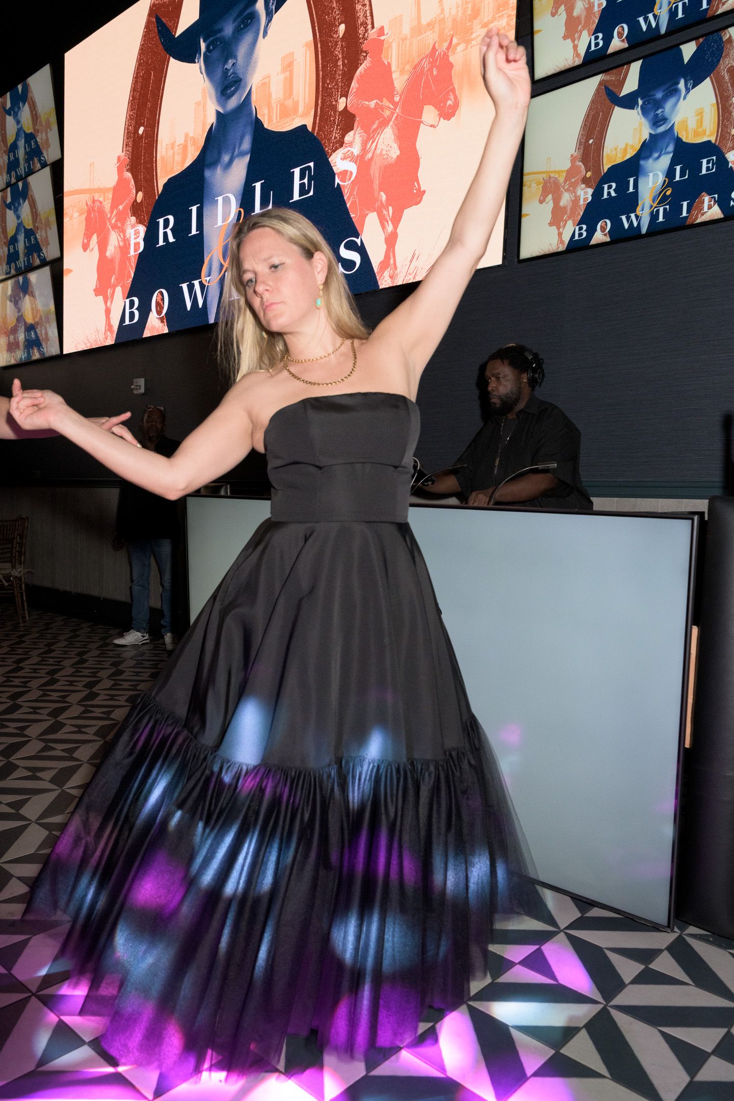 Woman in black strapless ball gown dances at Bridles and Bowties charity event with DJ in background.