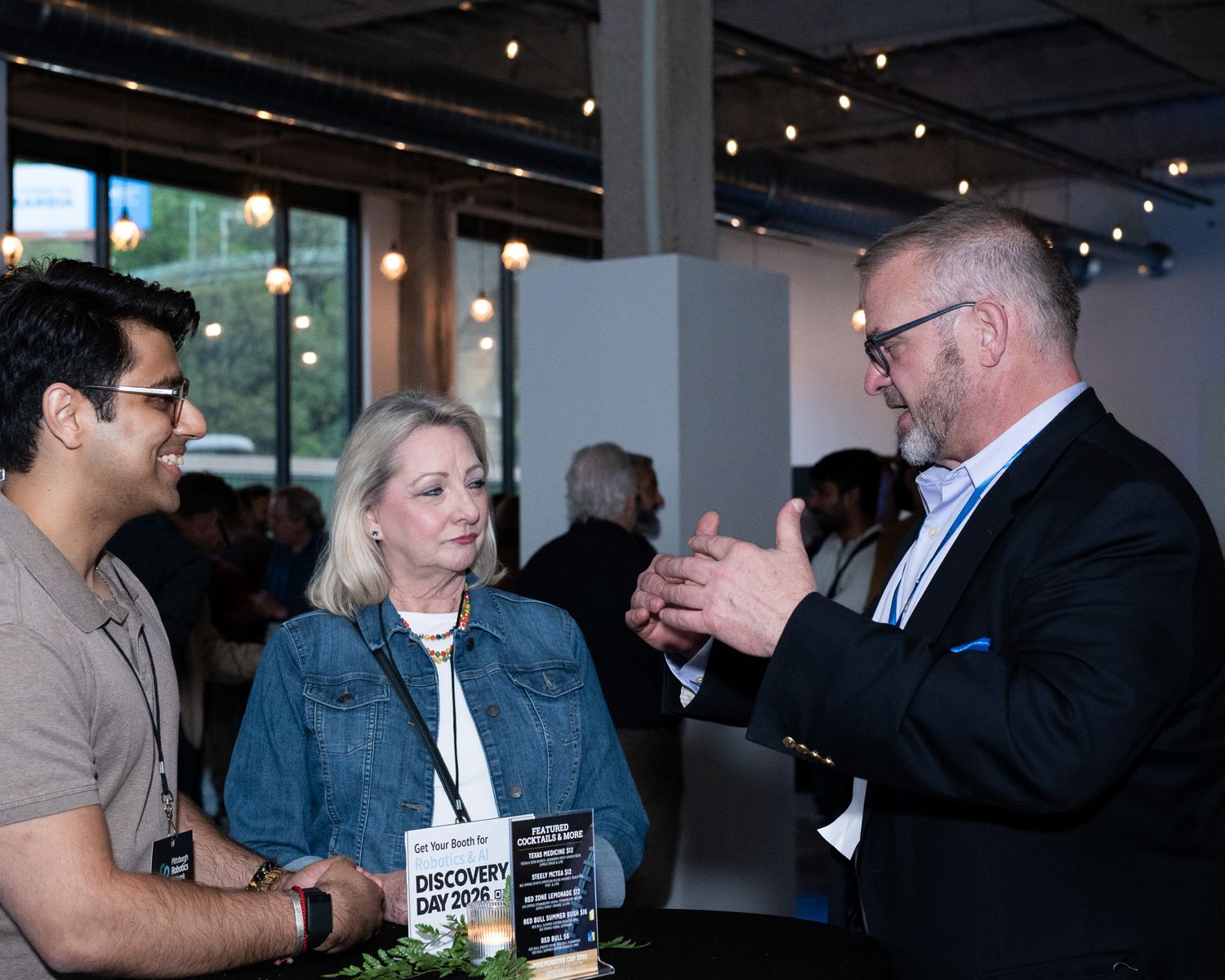 Three professionals networking at a Discovery Day event, engaged in conversation in a modern venue.