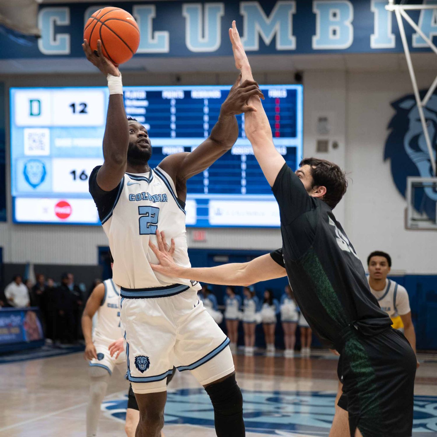 Columbia basketball player shoots over defender during competitive college game.