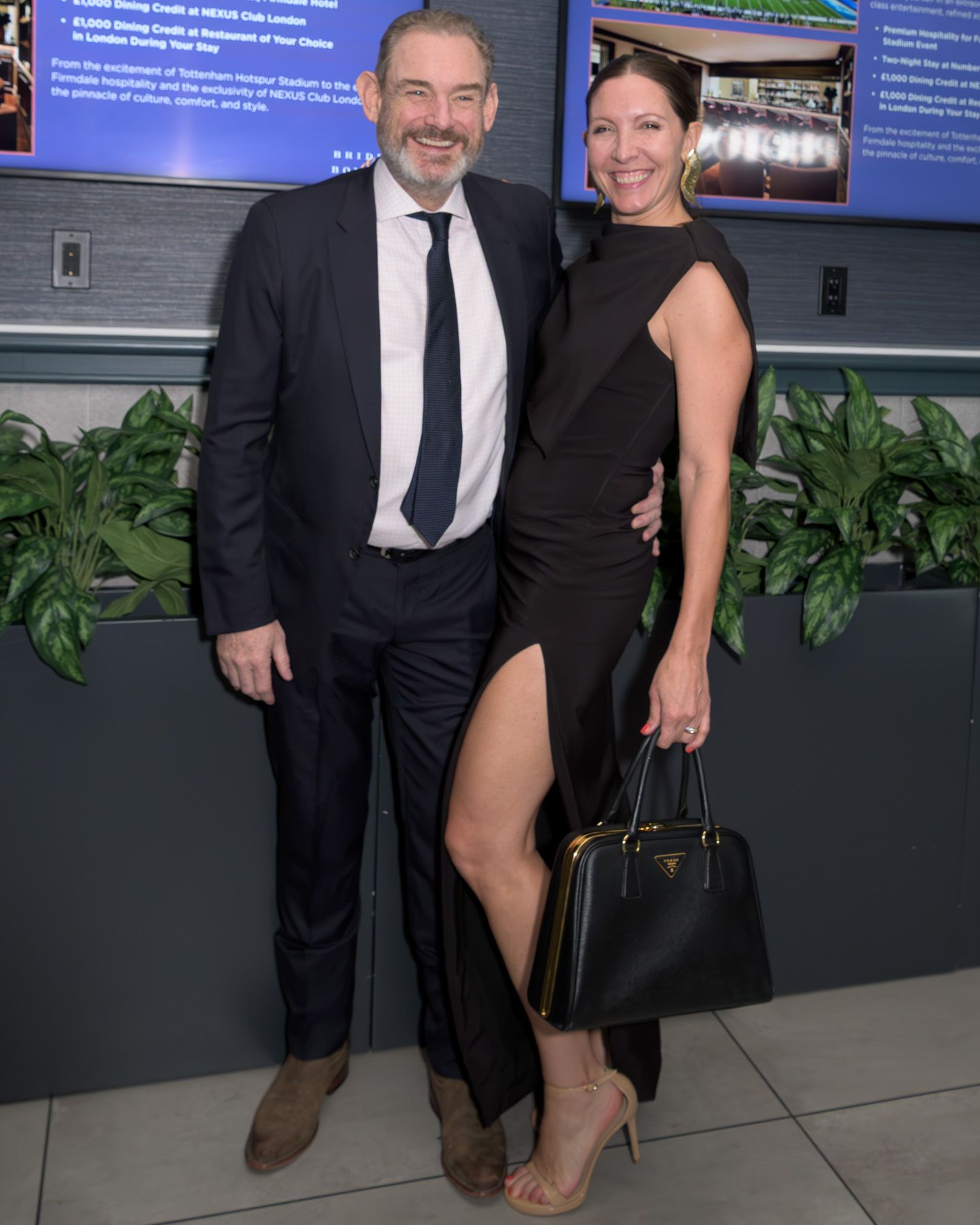 Couple posing together at formal event, woman in black slit dress holding Prada bag.