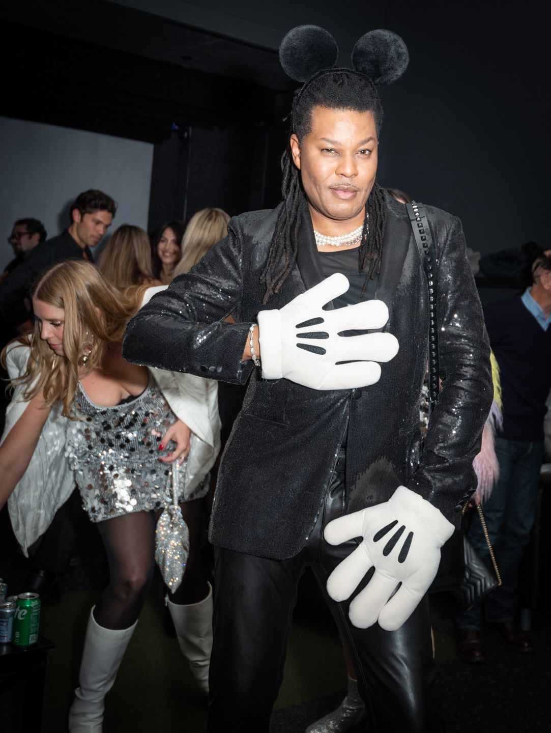 Person in Mickey Mouse ears and oversized white gloves posing at a nightclub event.