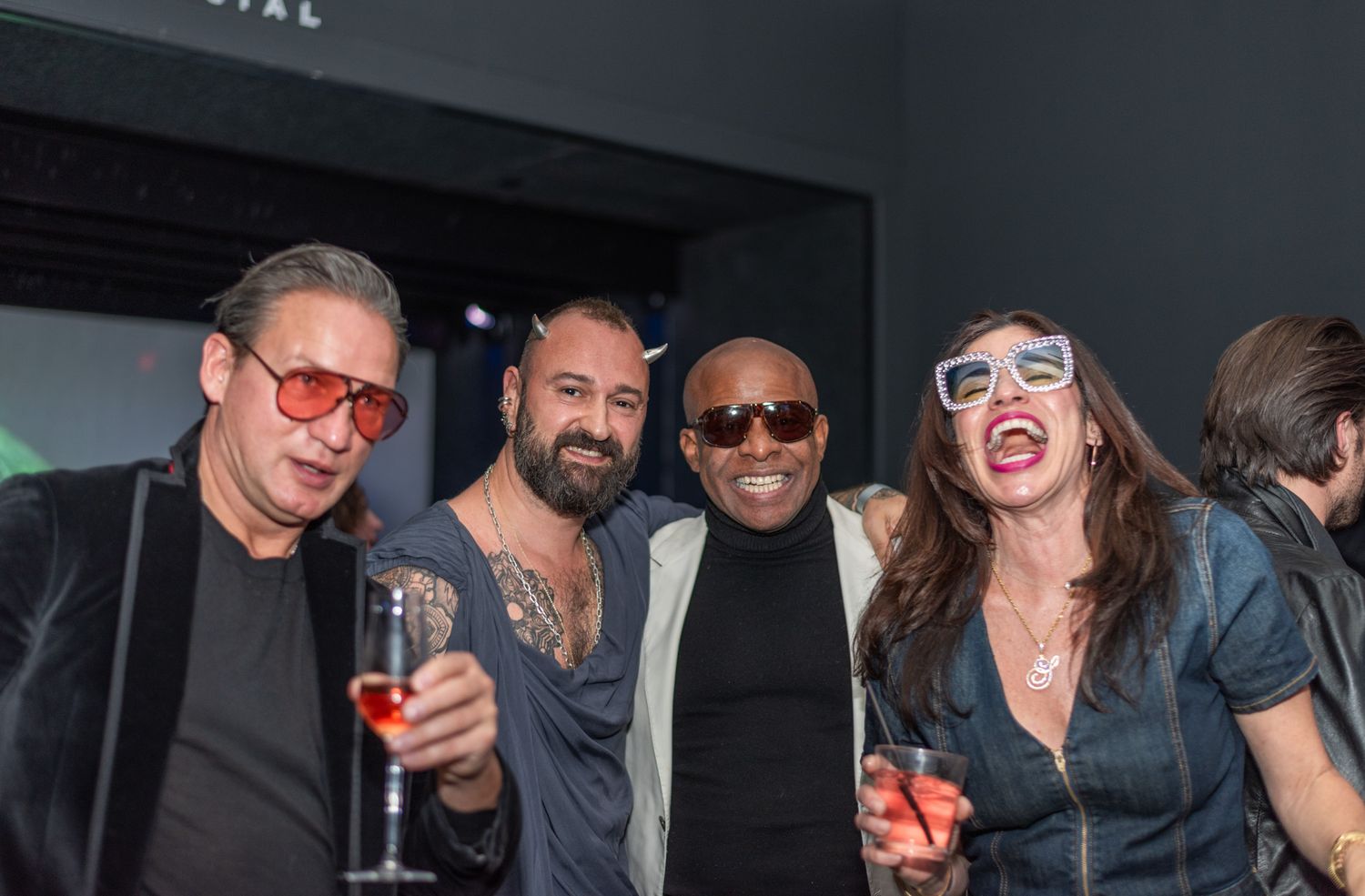 Four friends posing together with drinks at a stylish nightclub event wearing festive accessories.
