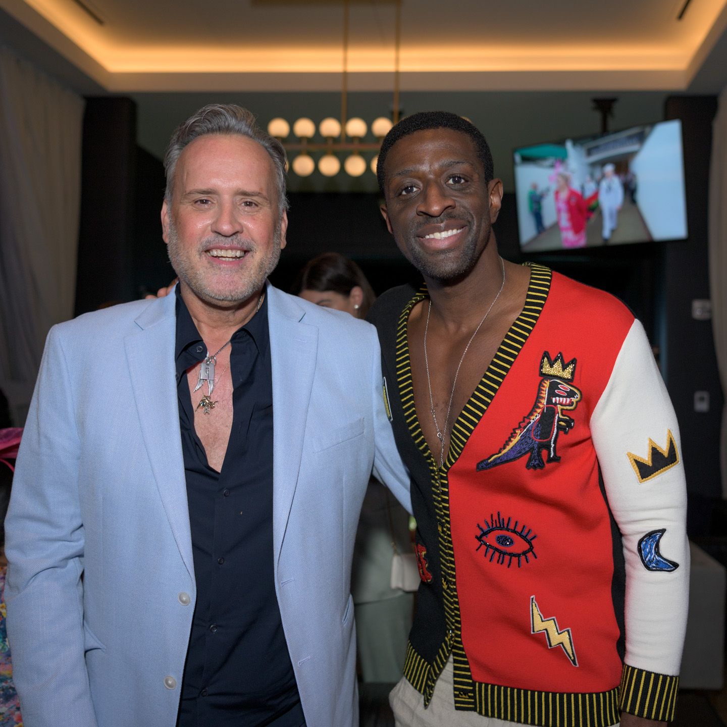 Two well-dressed men posing together smiling at an indoor social event.