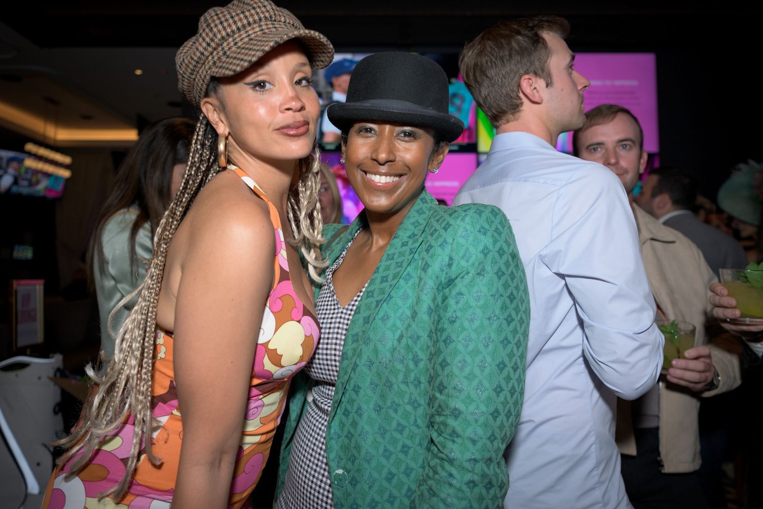 Two women posing together at a vibrant social event, one in green jacket.
