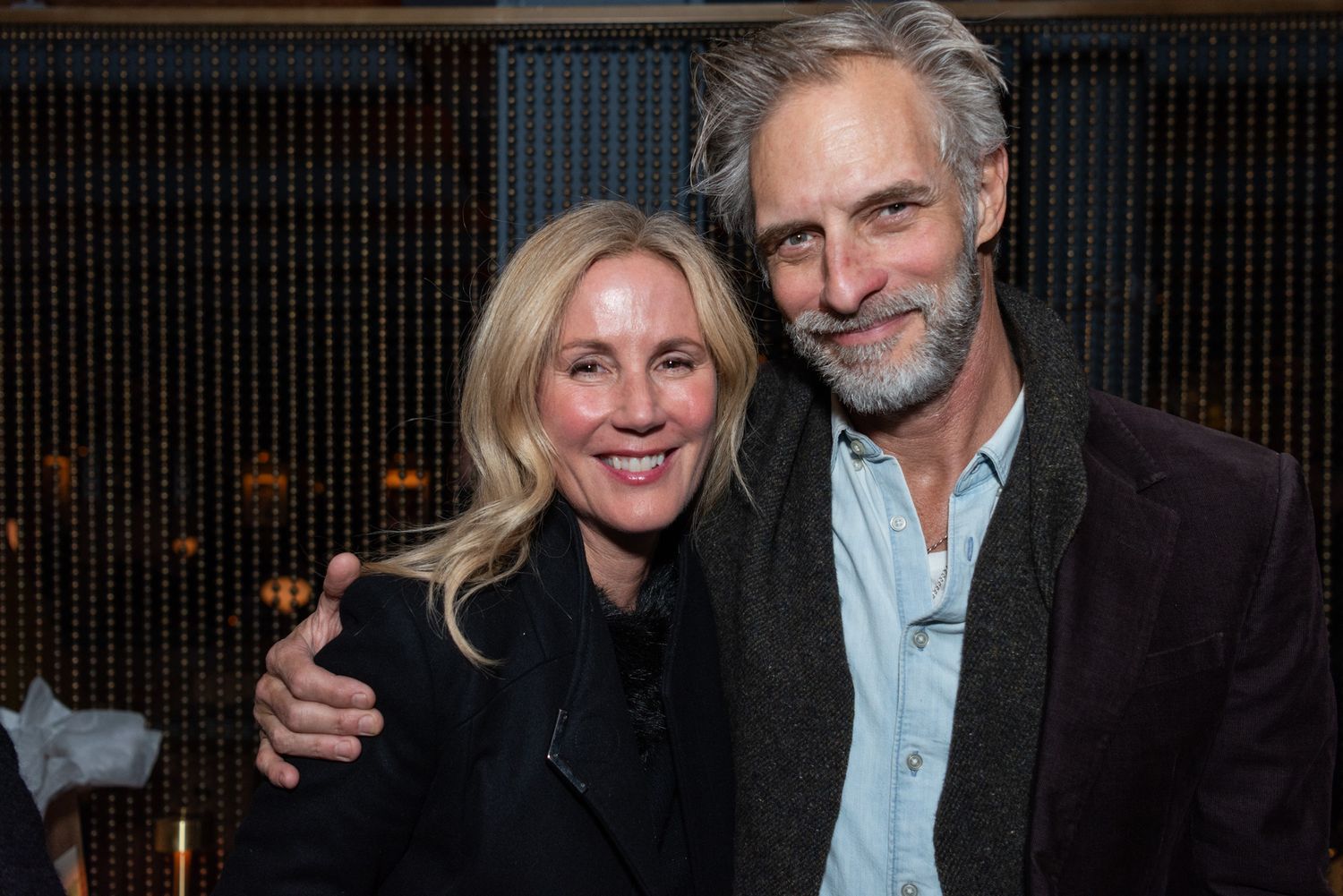 A smiling couple poses closely together at a dimly lit evening social event.