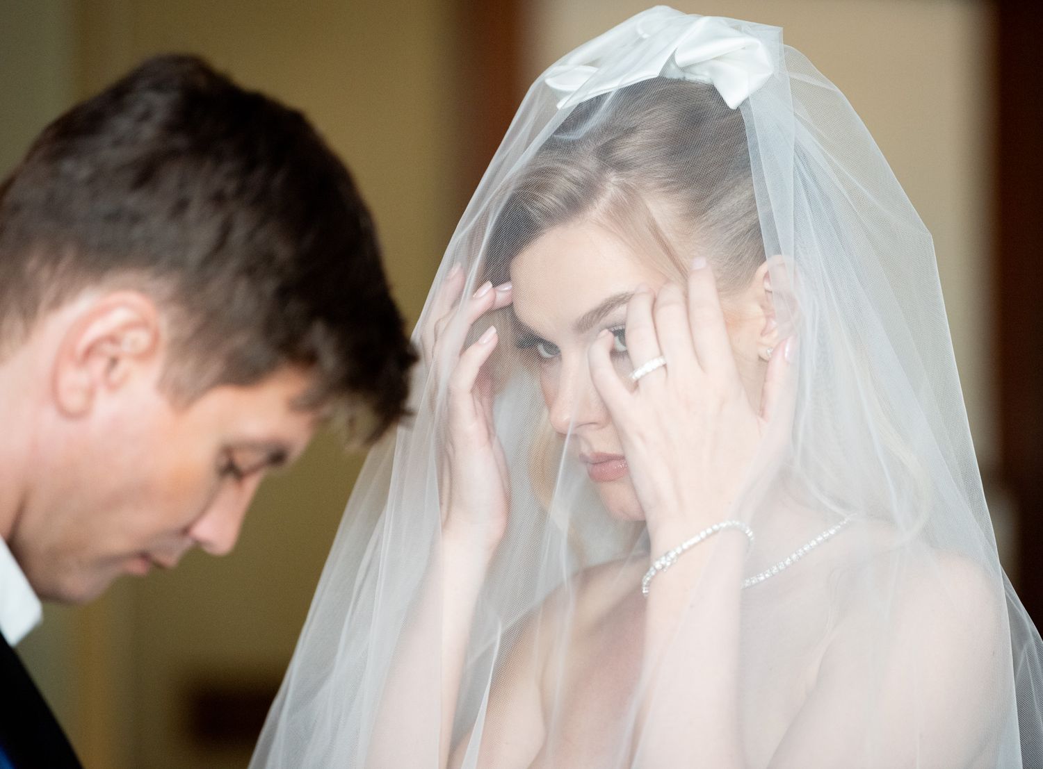 Bride adjusting veil while groom looks down during emotional wedding ceremony moment.