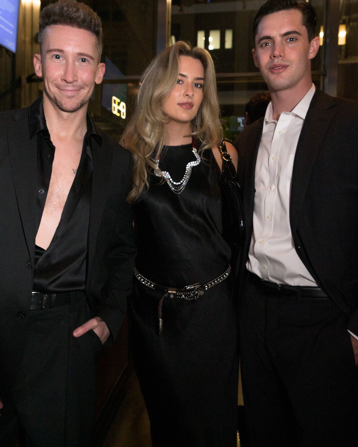 Three young people dressed in black pose together at an elegant evening event.
