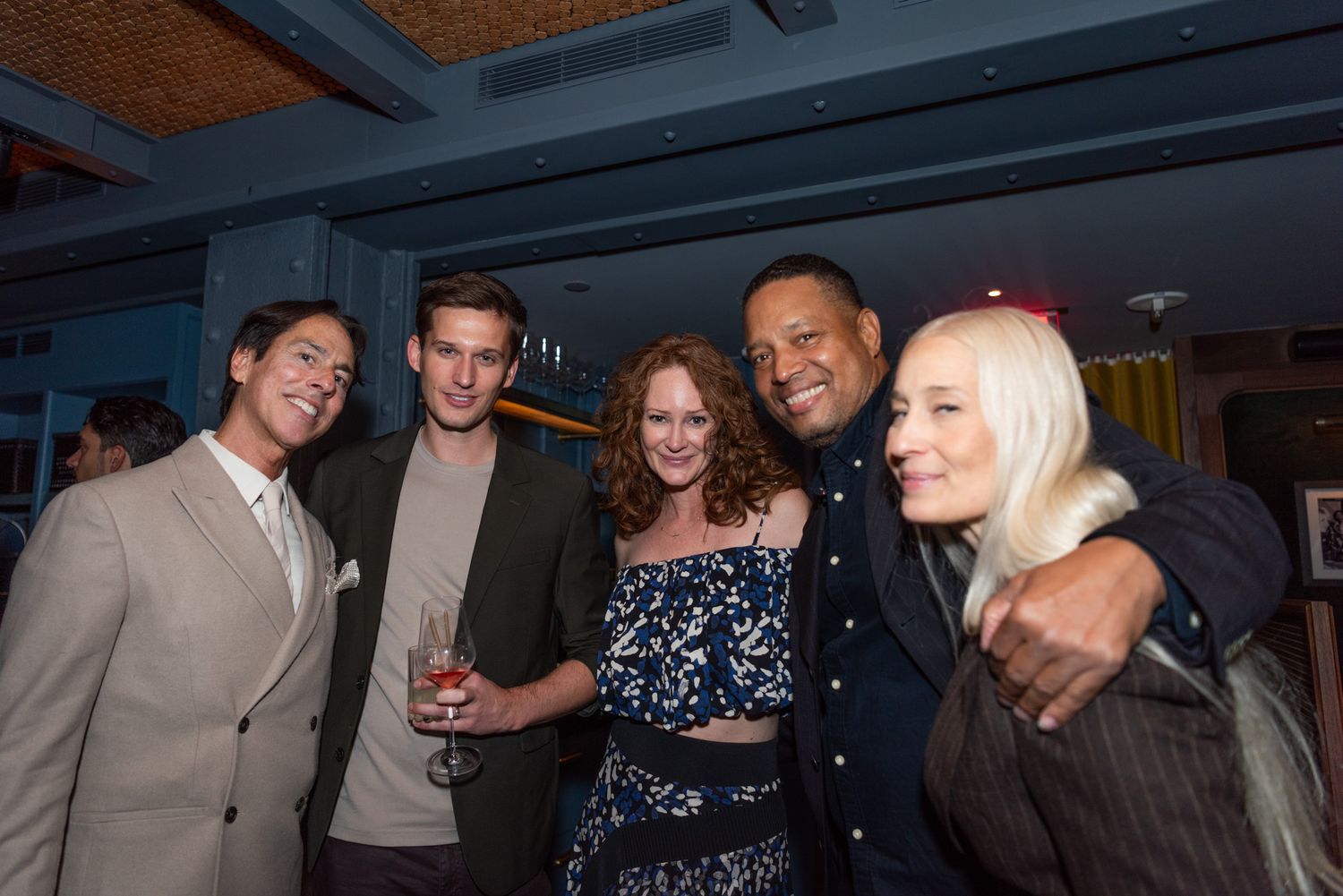 Five people smile and pose together at a casual indoor social event or party.