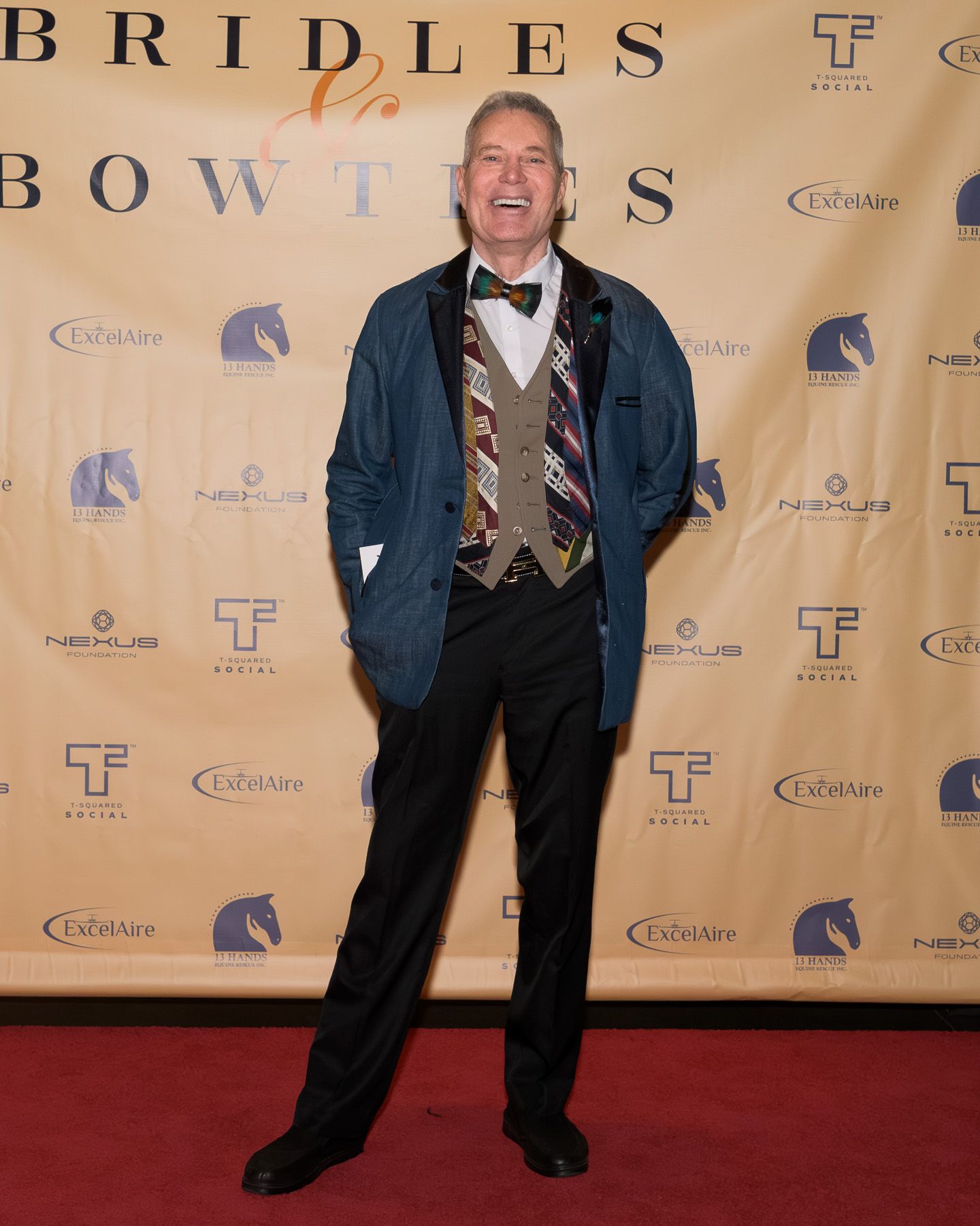 Cheerful man in colorful bow tie posing on red carpet at Bridles and Bowties event.