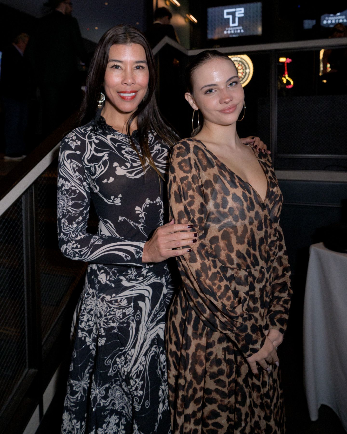 Two women in elegant dresses posing together at an indoor evening event.