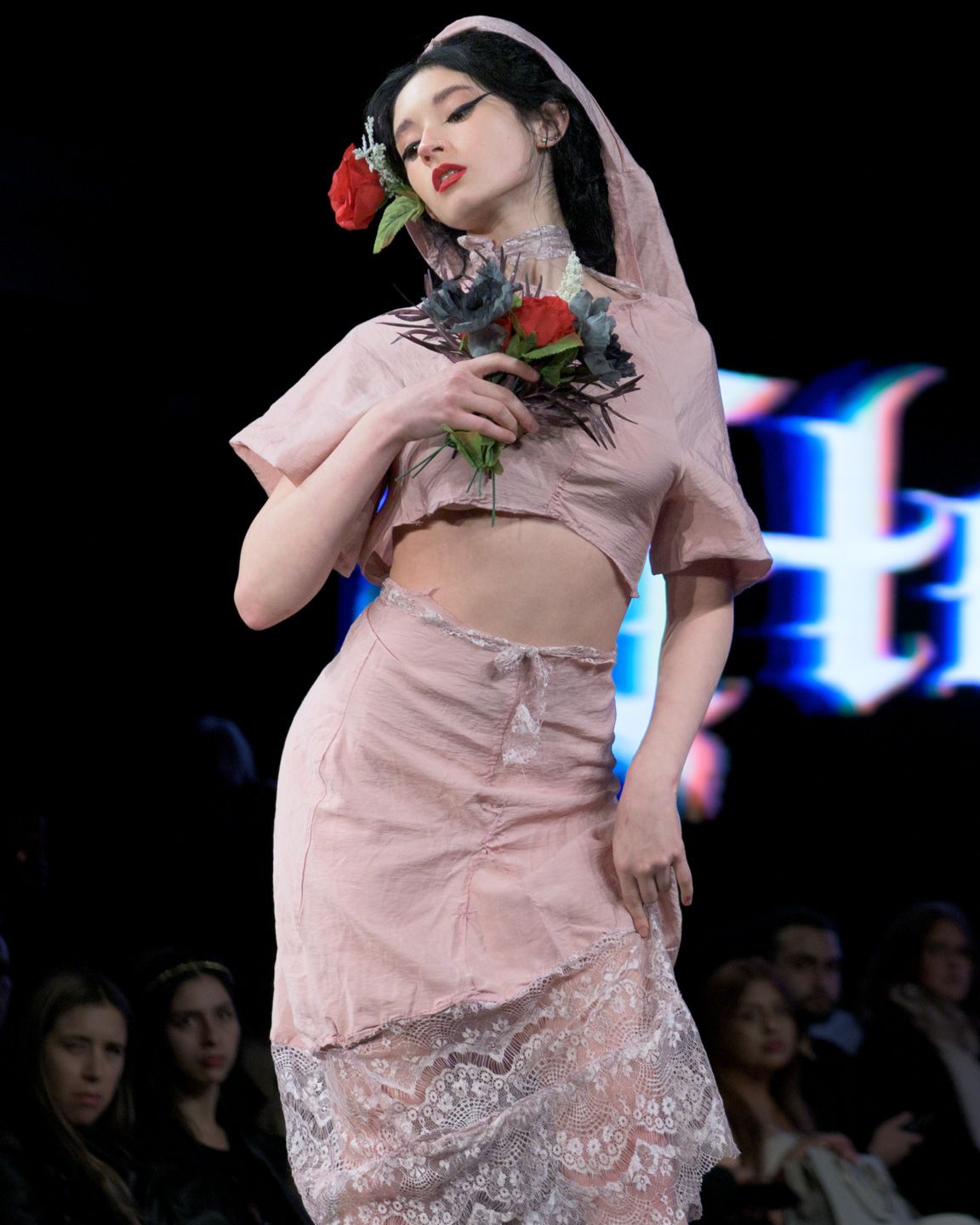 Model in pink crop set holds roses with floral head covering.