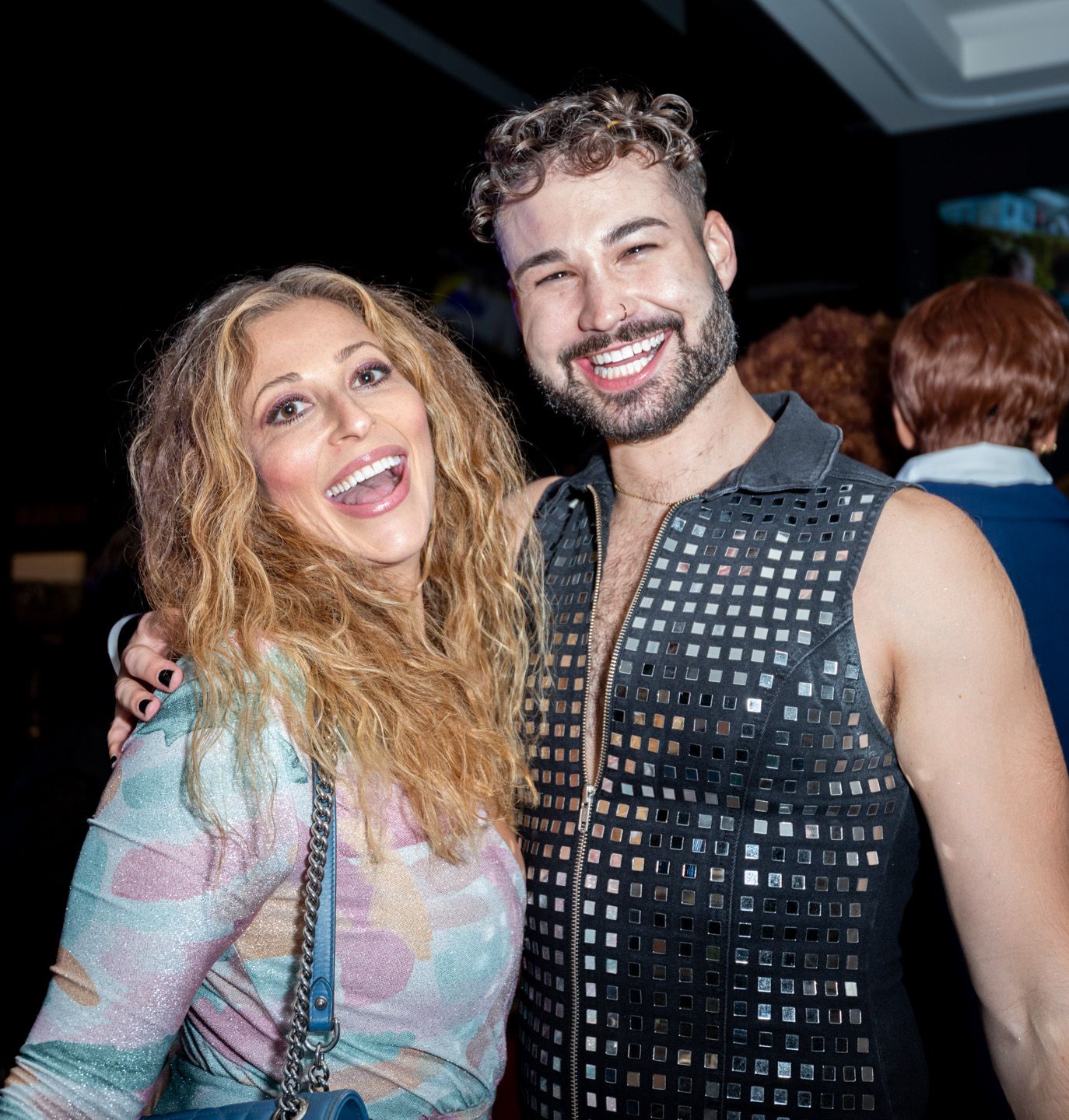 Smiling woman and man in studded vest pose together at a social event.