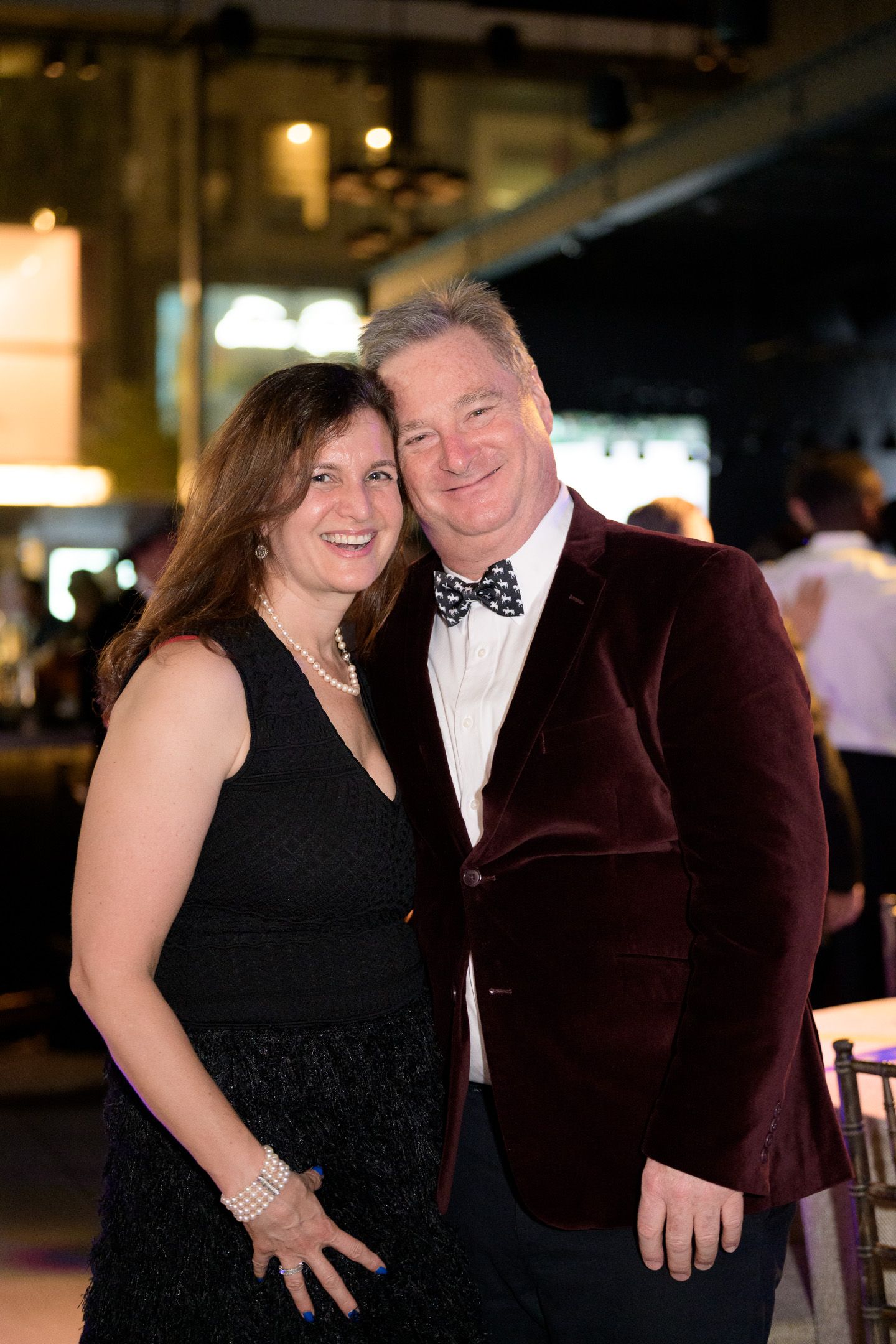 Smiling couple poses together at formal event, man in burgundy velvet blazer.