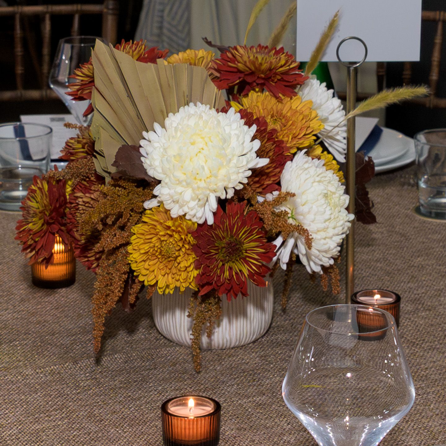 Autumn floral centerpiece with chrysanthemums and candles on a burlap table runner.