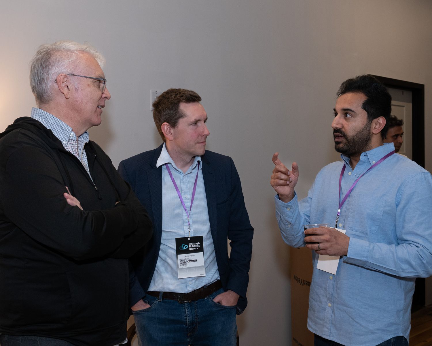 Three businessmen in discussion at a professional networking event with purple ambient lighting.