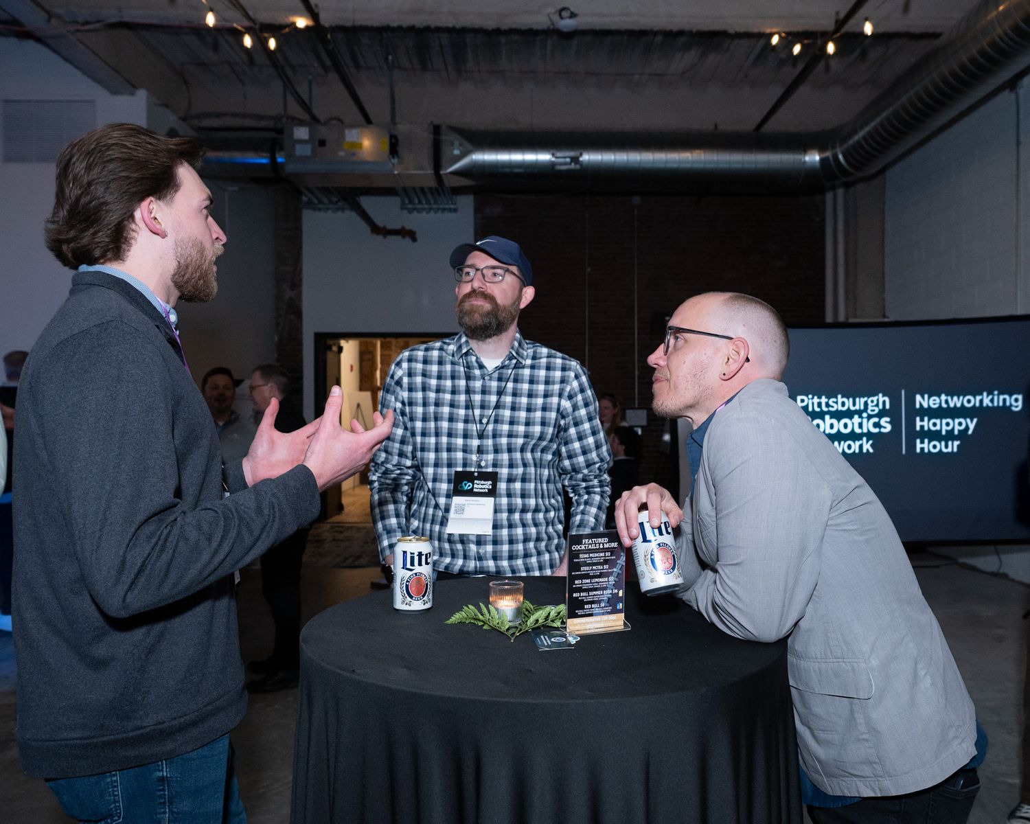 Three men networking at Pittsburgh Robotics Network Happy Hour around a high-top table.