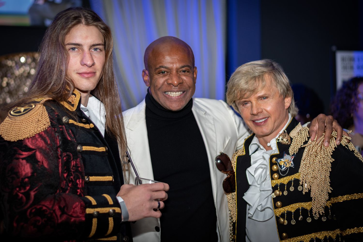 Three men in elegant costumes pose together at a formal evening event.