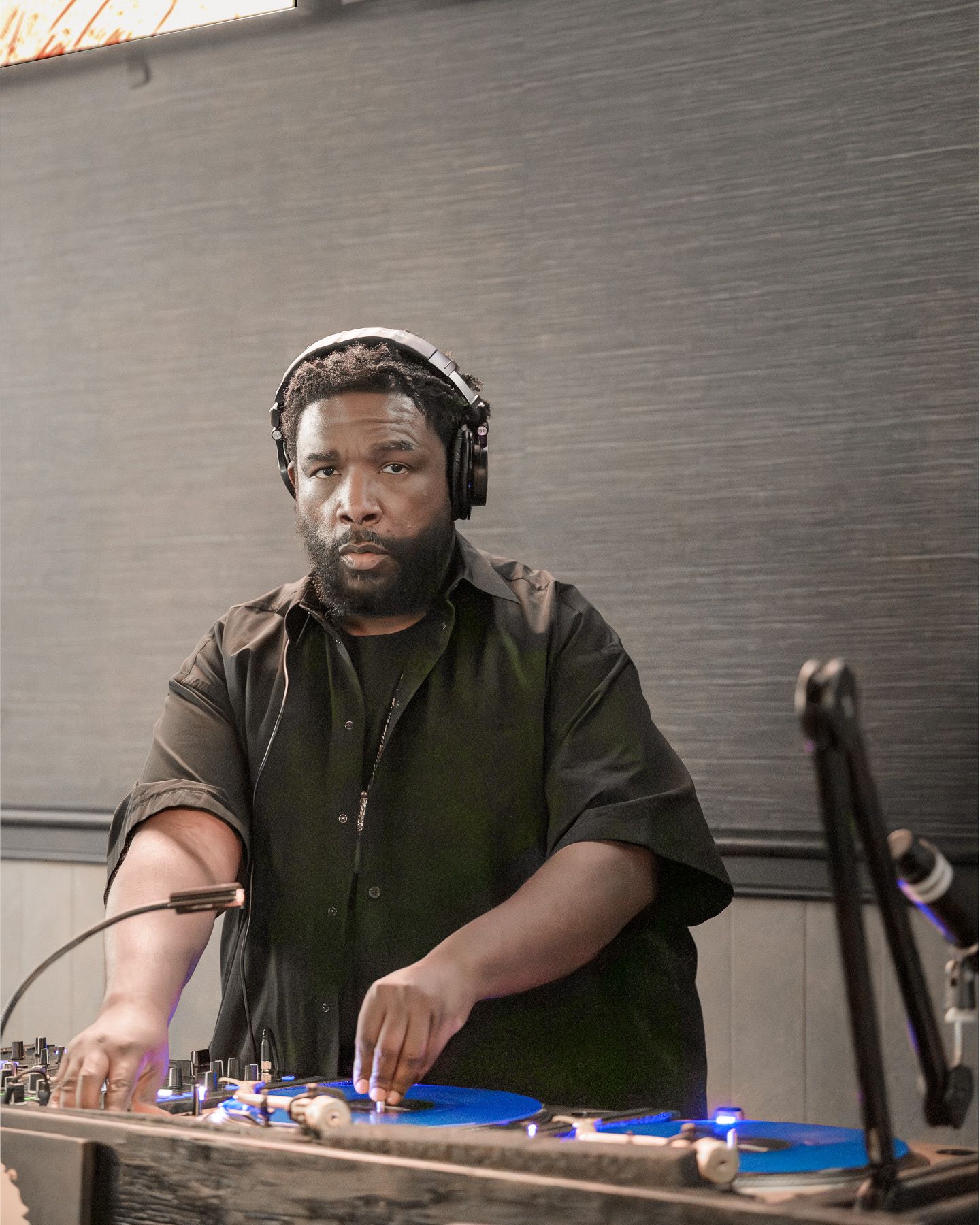 A DJ wearing headphones operates turntables with blue vinyl records in a dimly lit venue.