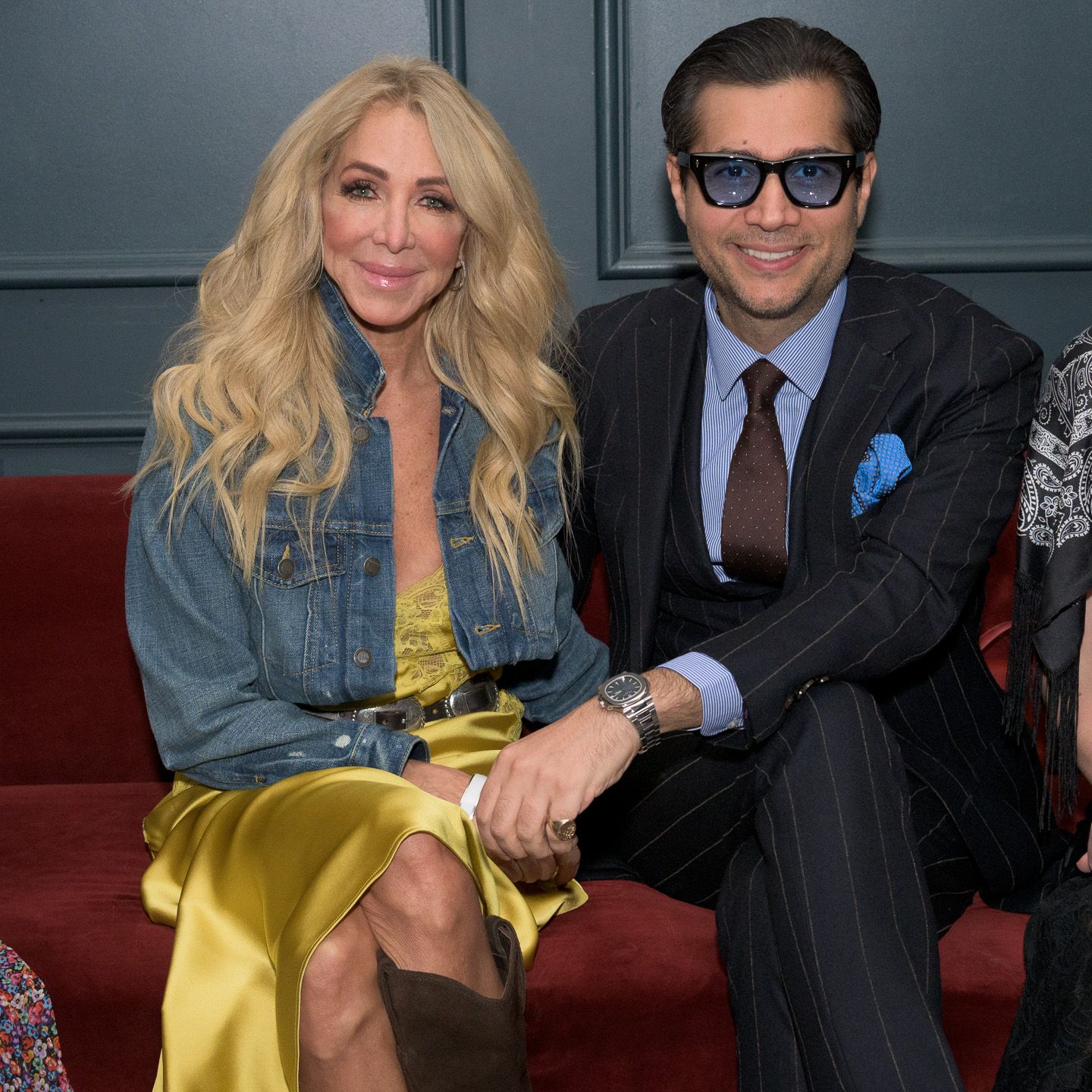 Blonde woman and suited man pose together on red sofa.
