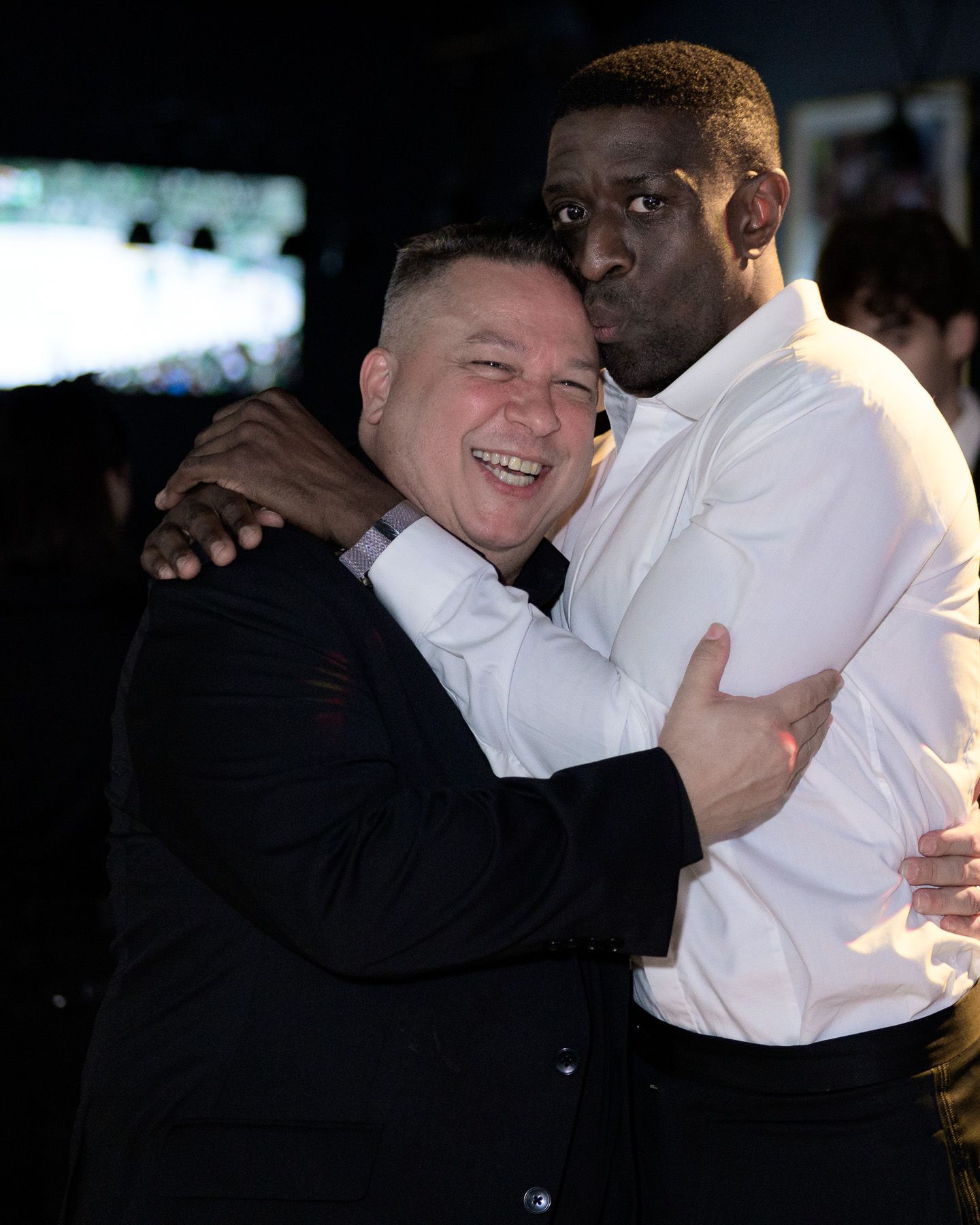 Two men share a warm embrace and laugh at evening celebration.
