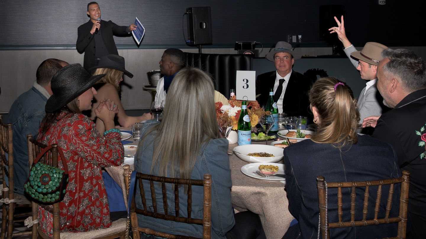 Guests enjoy a formal dinner gala while a speaker presents on stage at a Bridles and Bowties charity event.
