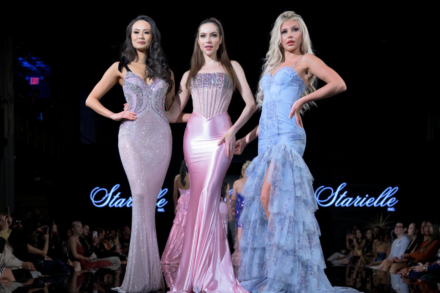 Three models pose in elegant sequined and ruffled formal gowns on Starielle runway.