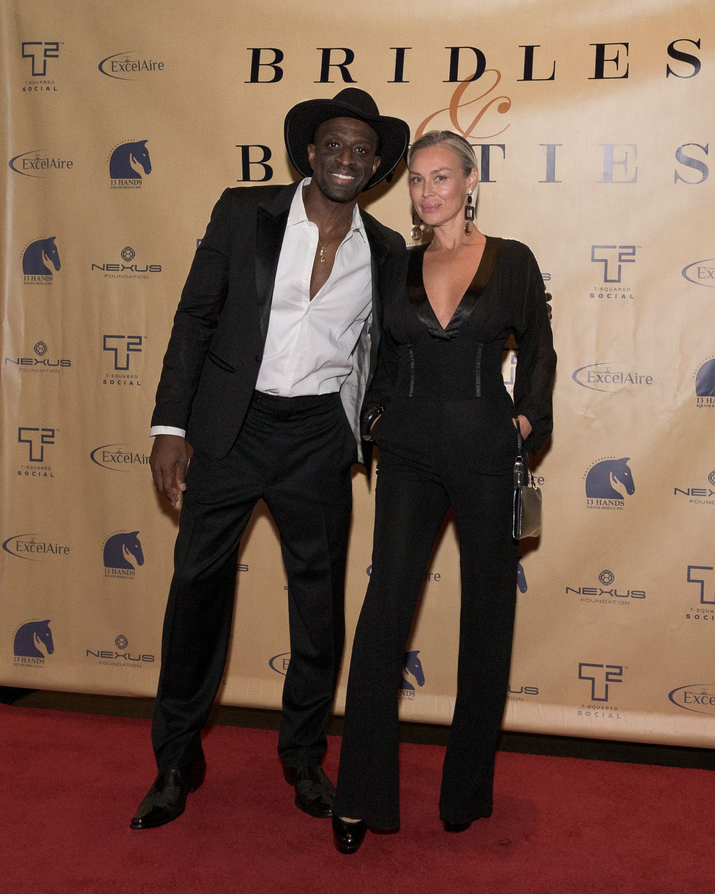Stylish couple poses on red carpet at Bridles and Booties event.