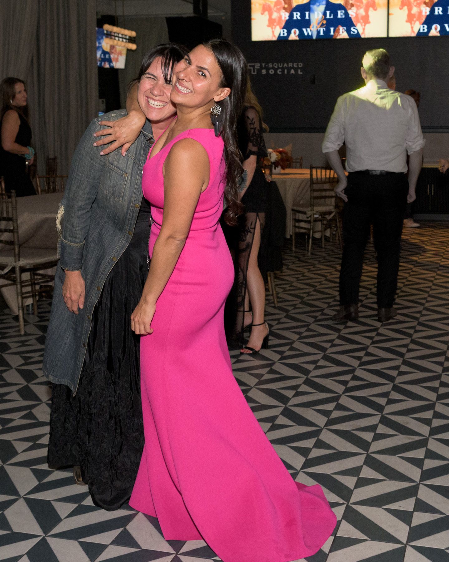 Two women pose together at Bridles and Bowties gala, one in pink gown and one in gray jacket.