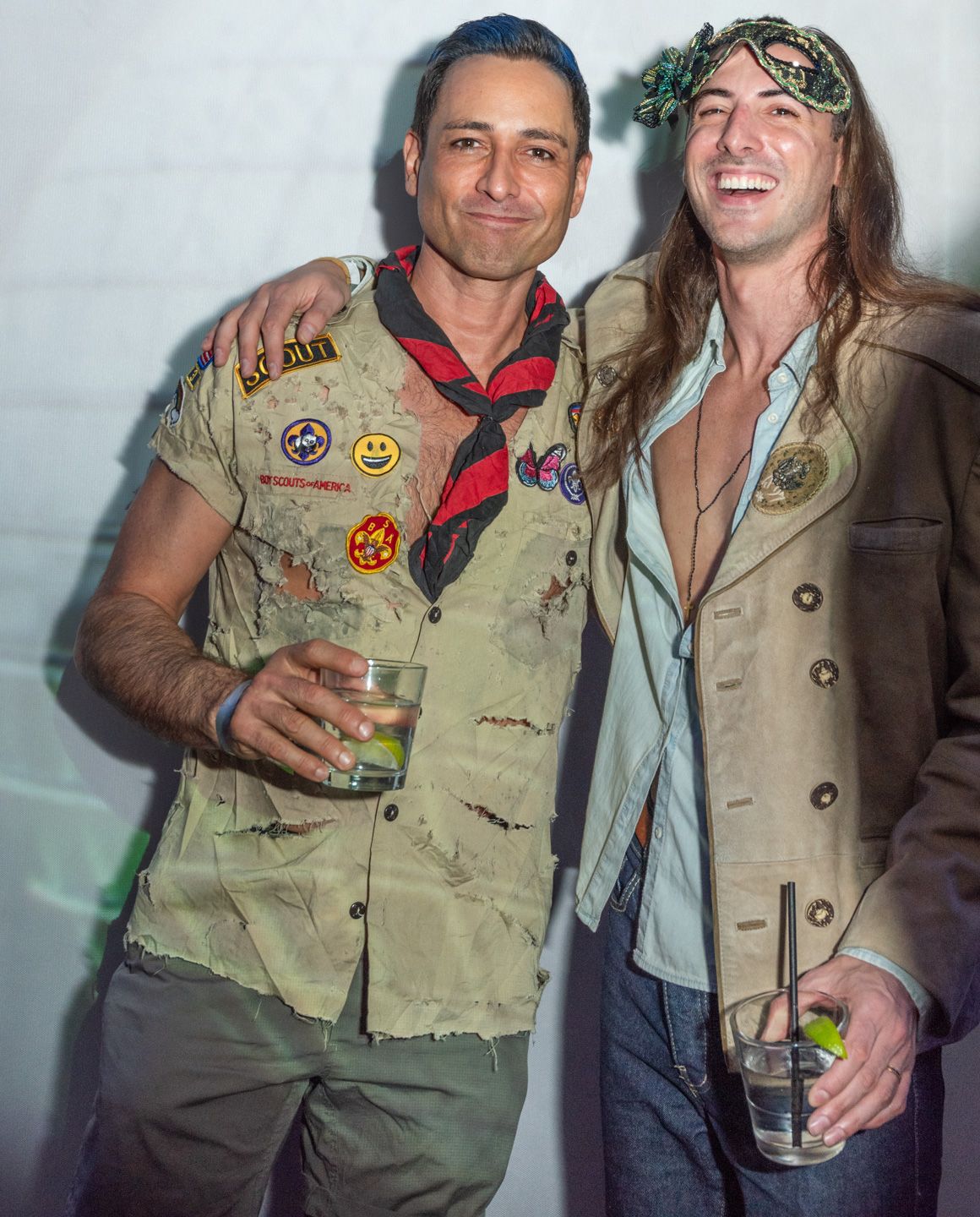 Two men in Halloween costumes posing together holding drinks at party.